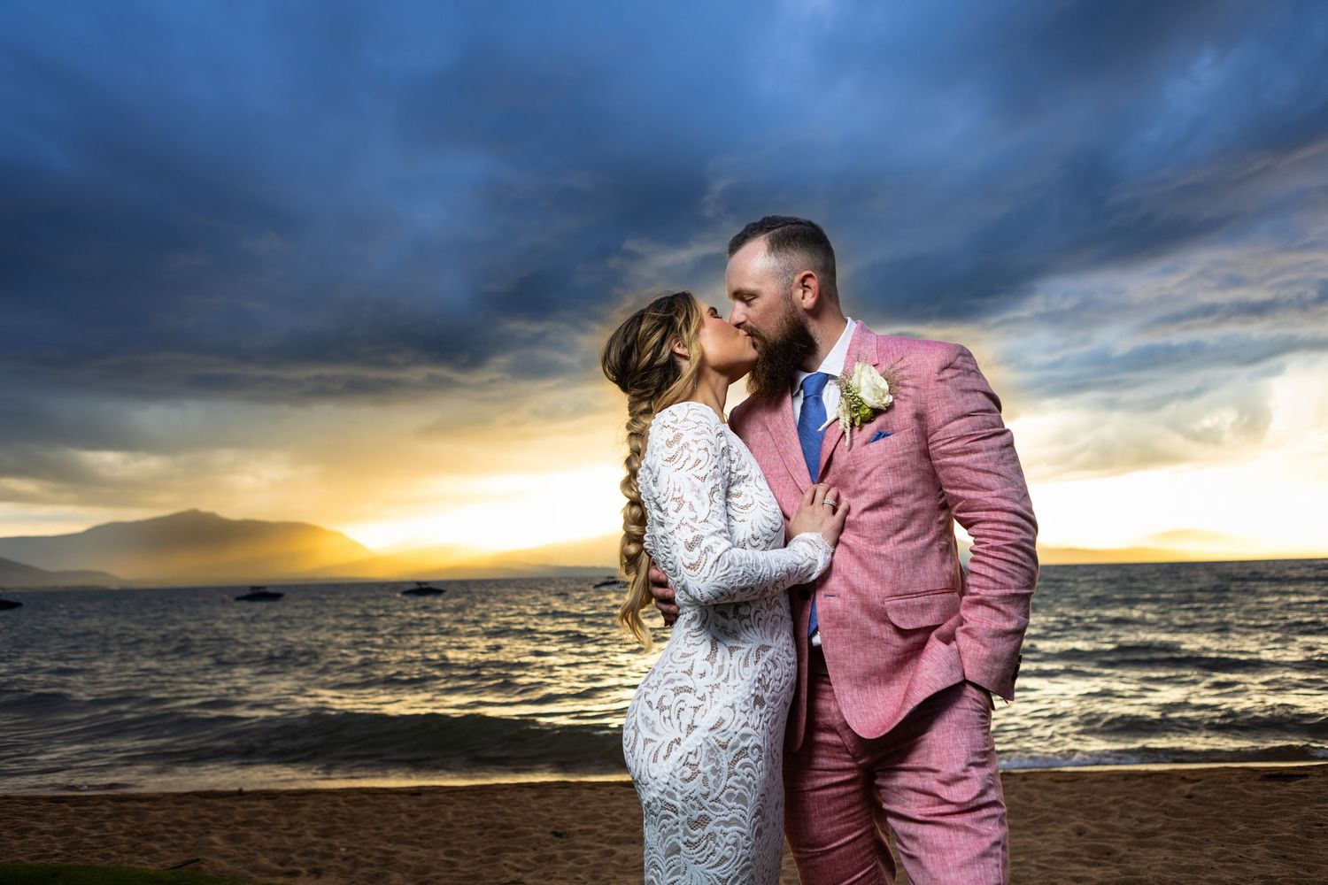 A sunset beach wedding photo with dramatic clouds and mountains in the background.