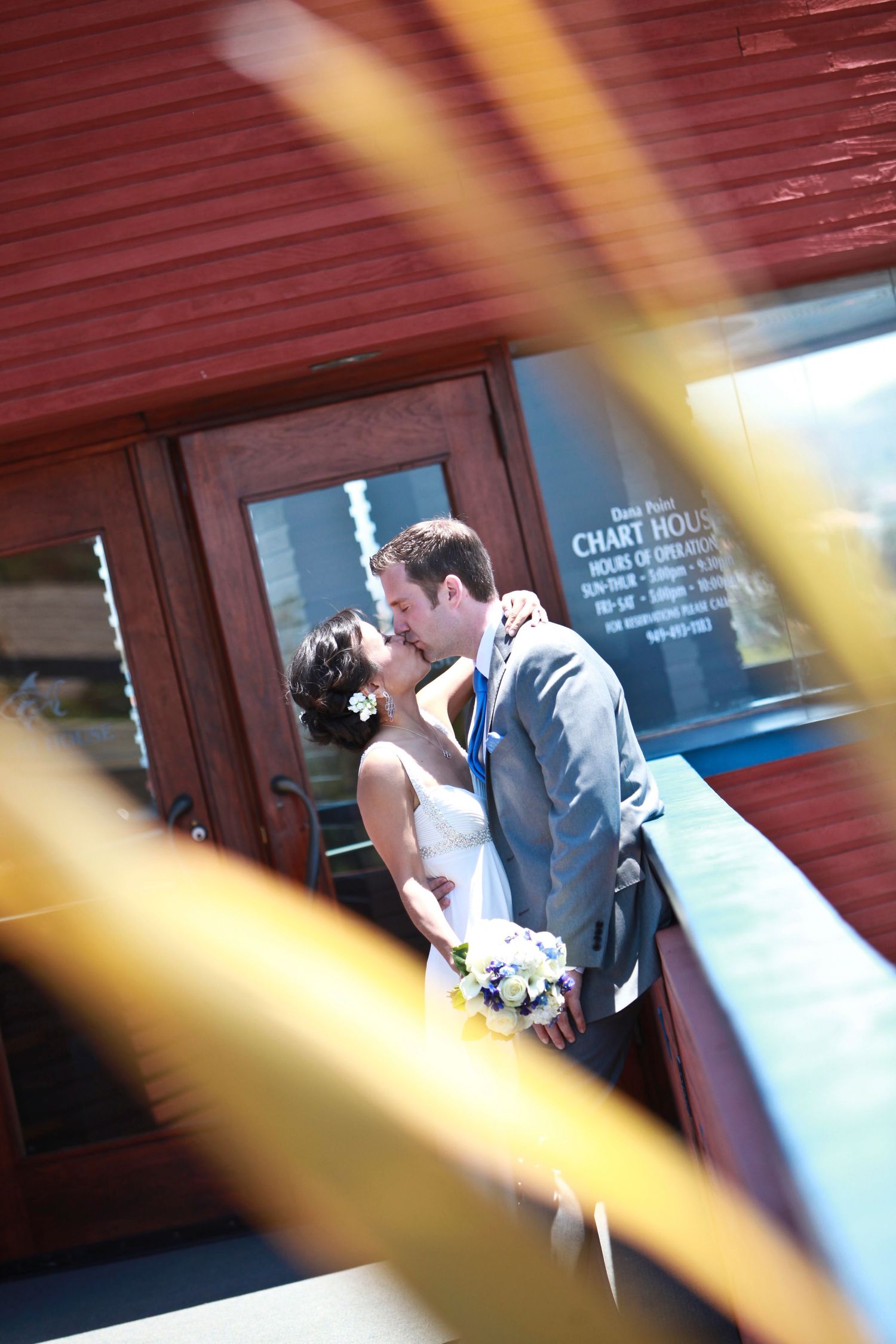 Wedding couple sharing a kiss through window reflections with sunlight streaming through.