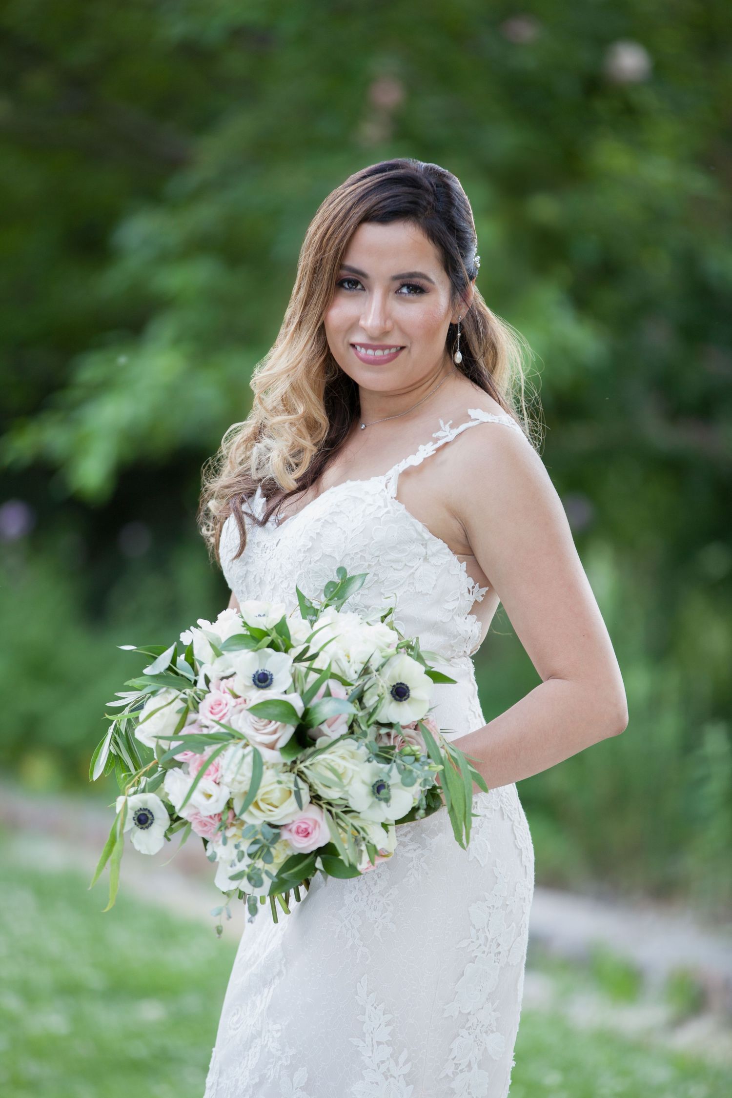 Elegant bridal portrait showcasing a white bouquet with anemones and roses against garden backdrop.