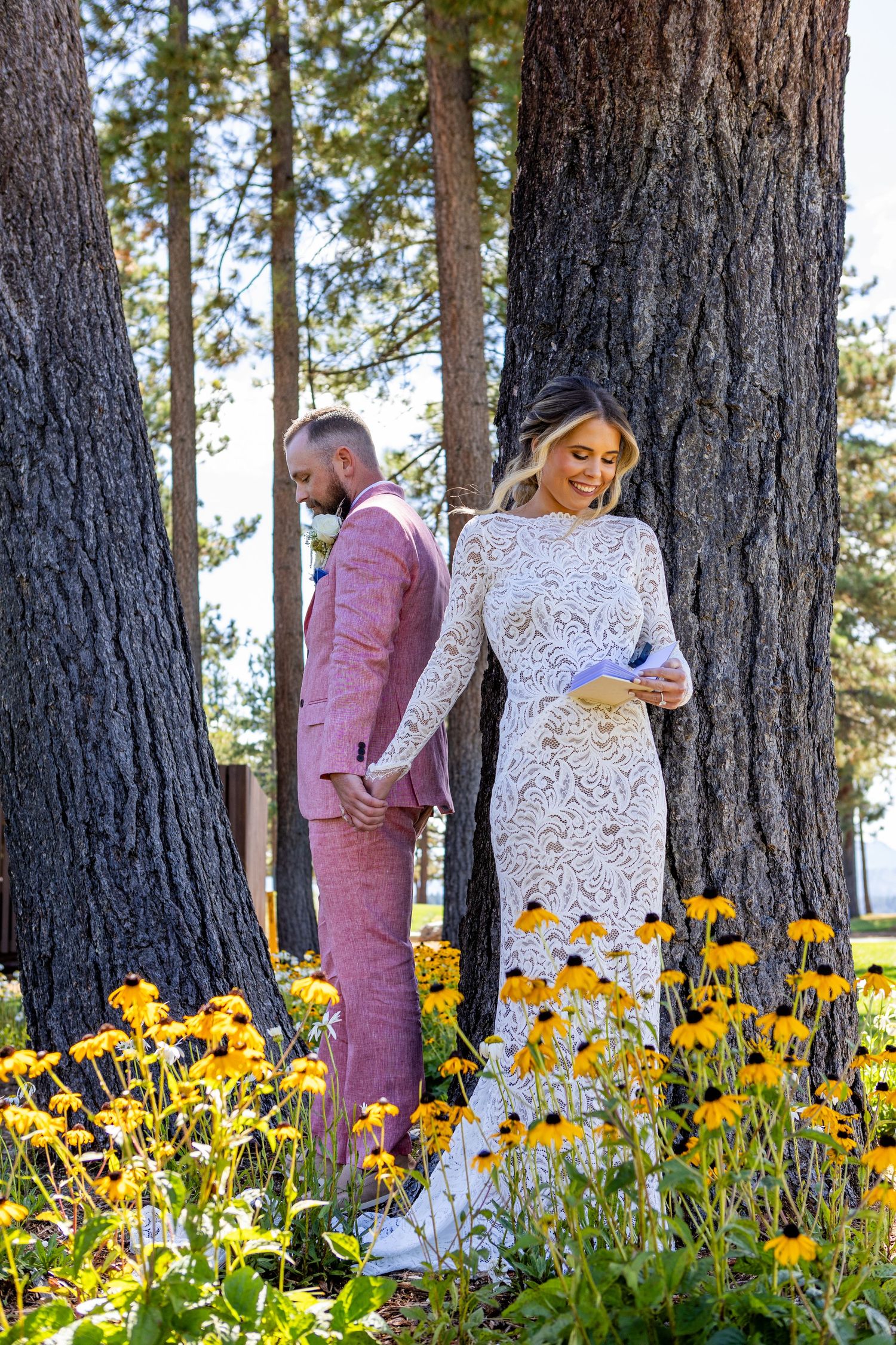 Wedding couple standing among yellow wildflowers and pine trees in an outdoor setting.
