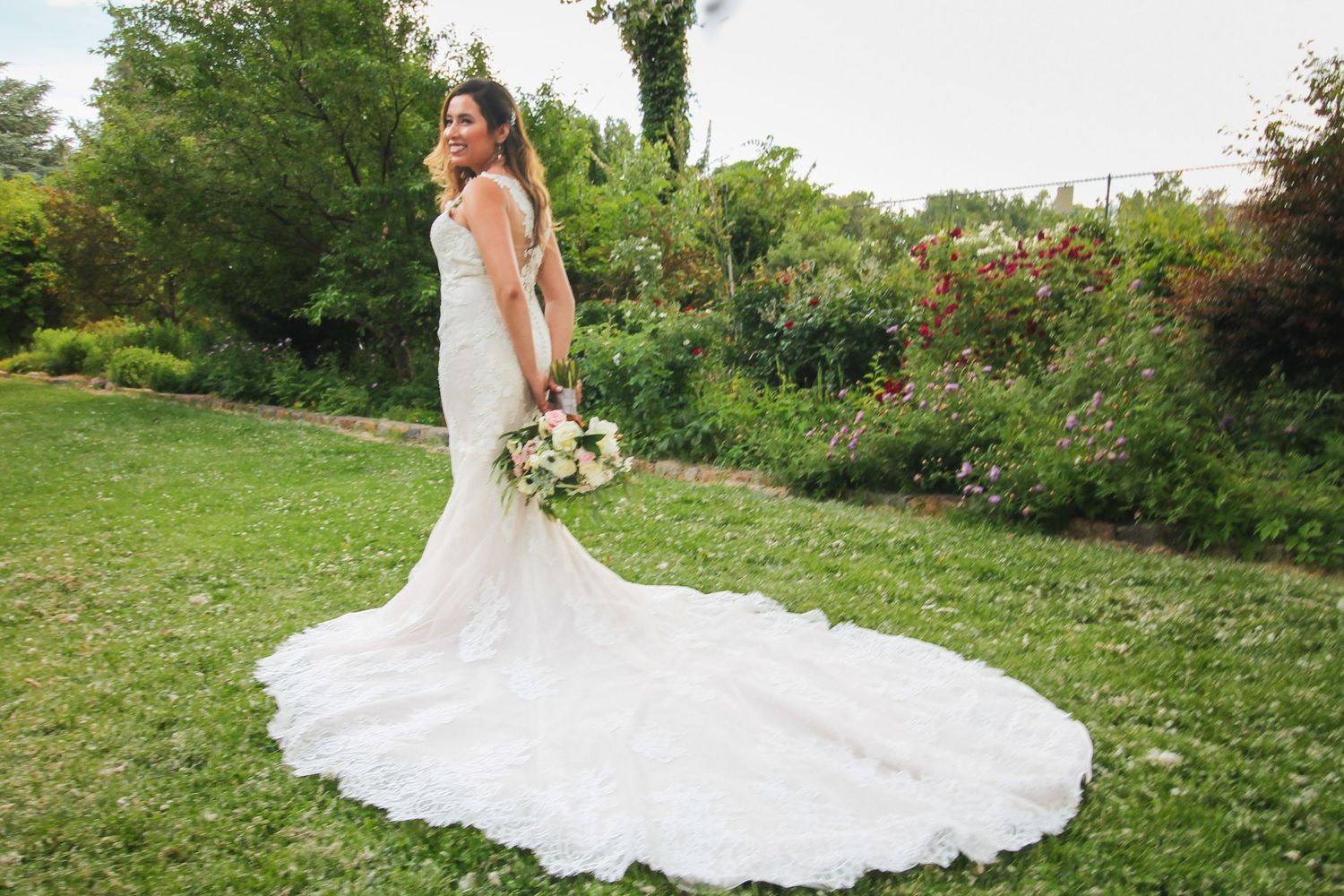 Beautiful wedding dress train trails across green grass in an outdoor garden setting.
