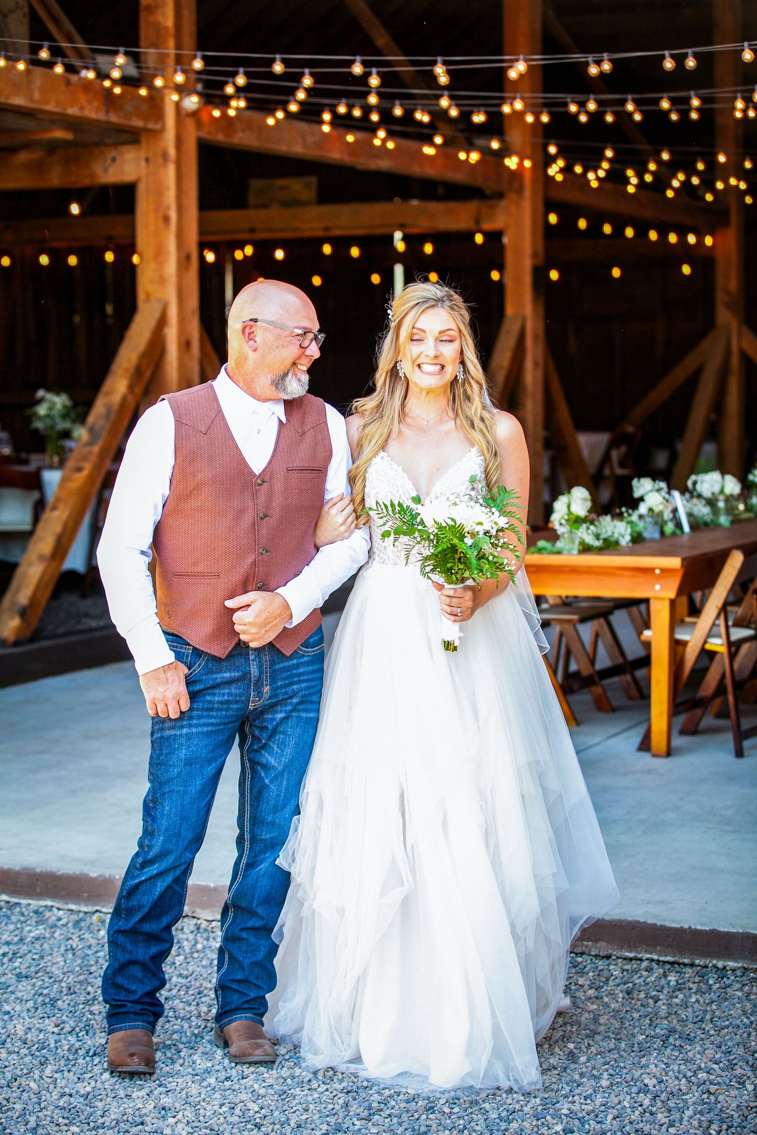 Wedding couple celebrates under string lights in rustic barn venue.