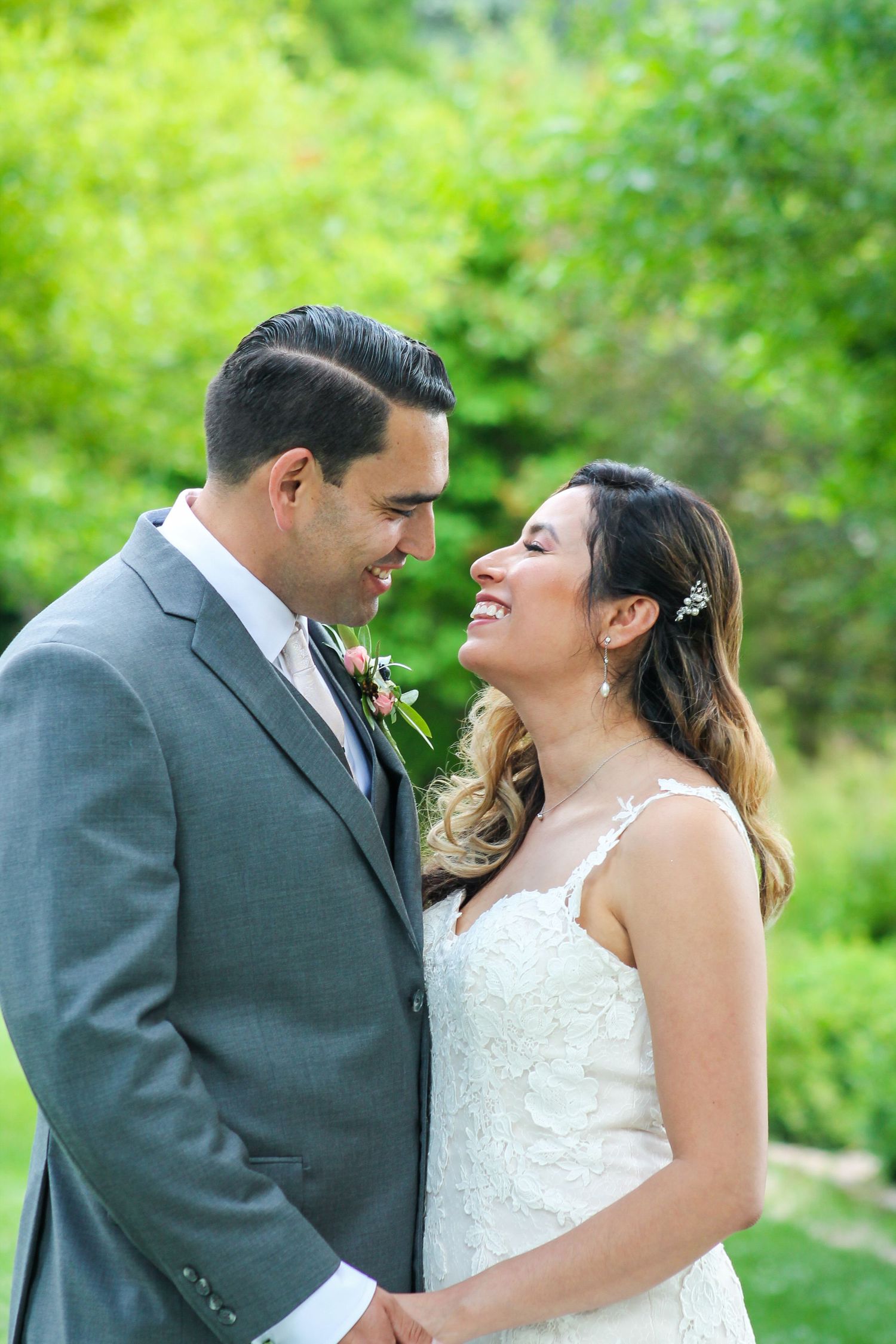 Happy couple laughs together during their wedding photoshoot in a green garden setting.