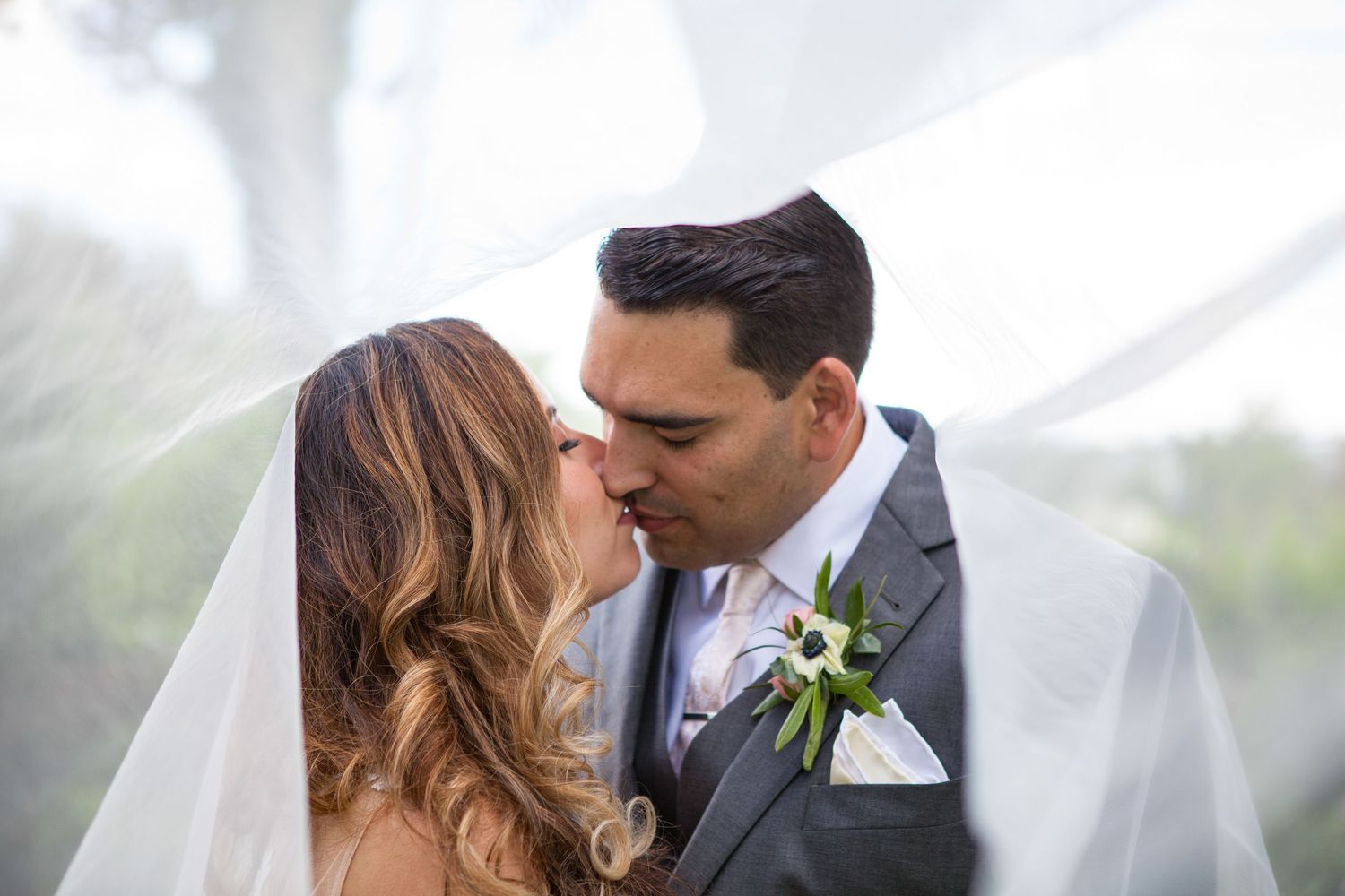 Romantic couple shares tender moment under flowing veil during garden wedding.