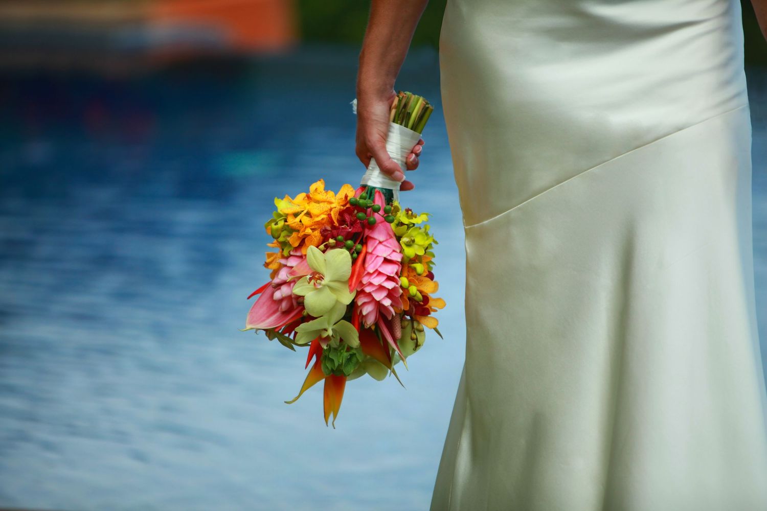 Colorful bridal bouquet with pink and orange flowers against a white wedding dress in Costa Rica.