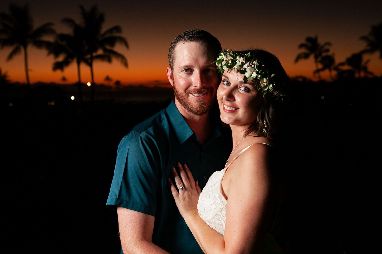 A couple shares romantic moments at sunset with palm trees silhouetted against an orange sky in Kauai.