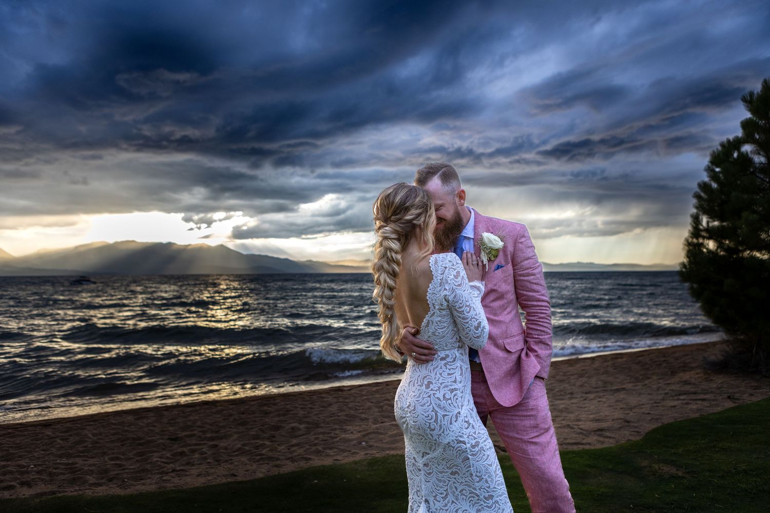 A romantic sunset beach wedding portrait with dramatic stormy skies and mountain backdrop.
