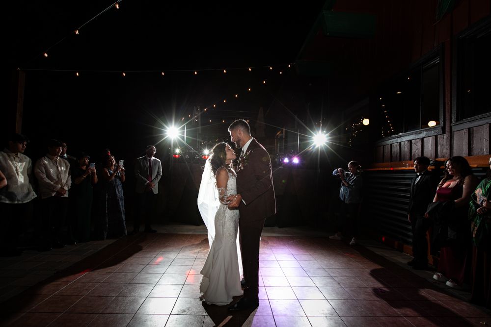 A couple shares their first dance at a wedding reception with dramatic spotlights illuminating the dance floor.