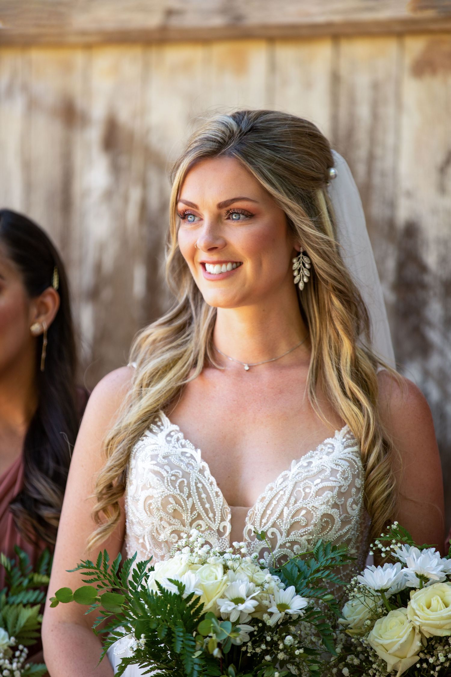 A bride in a detailed lace wedding dress holding a bouquet of white flowers and greenery.