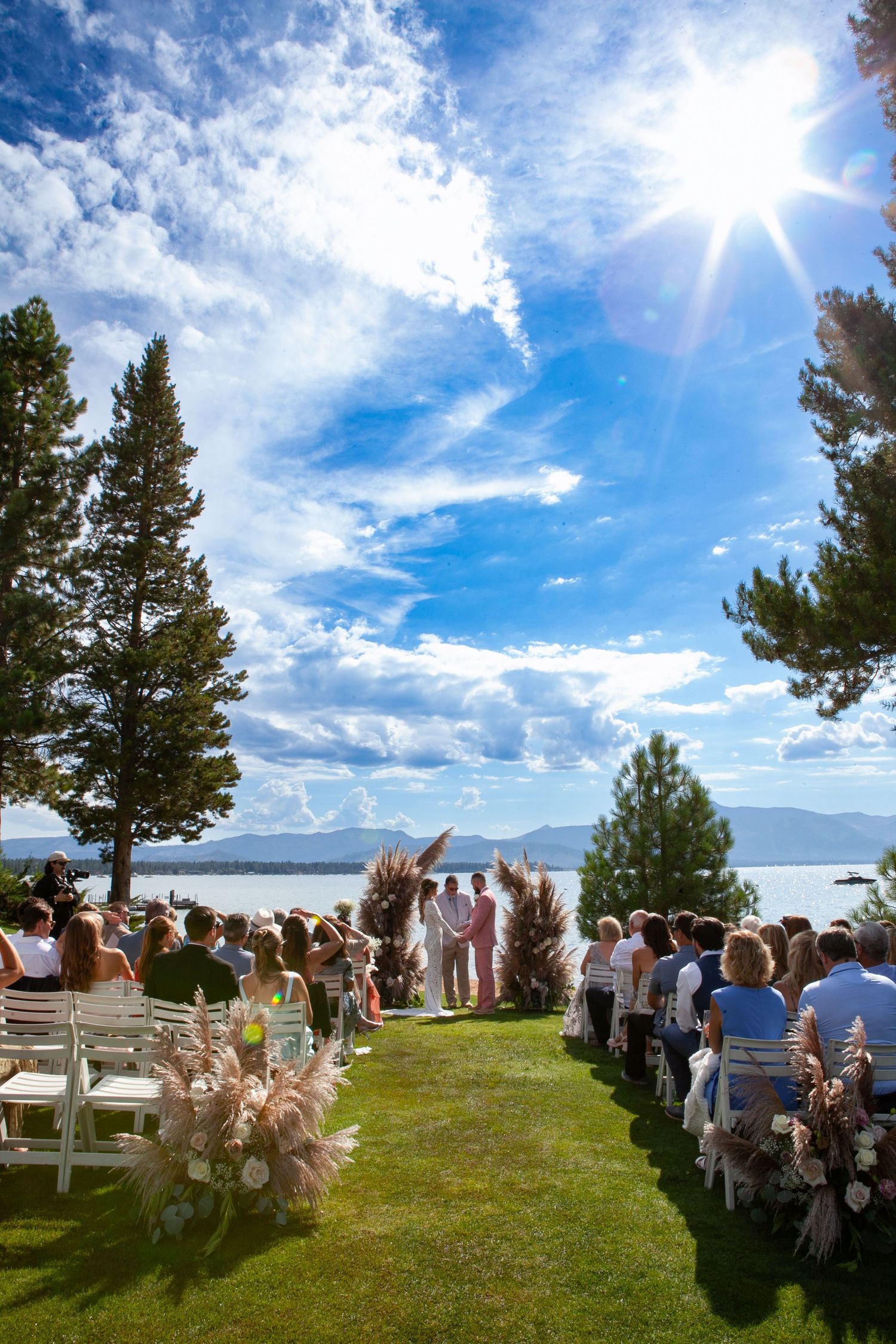 Outdoor wedding ceremony setup with white chairs overlooking a lake under bright blue skies.