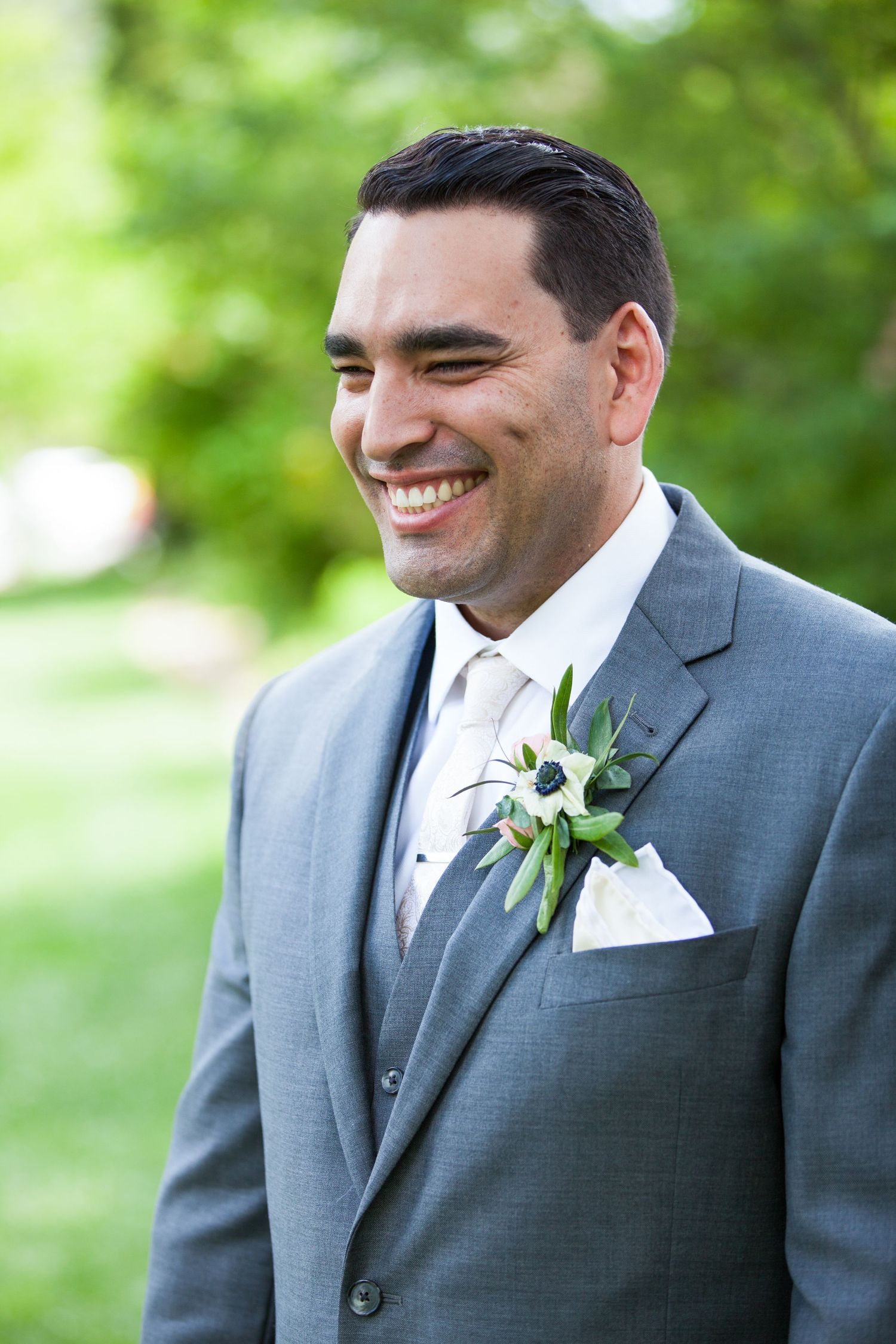 Groom in grey suit with white boutonniere smiles during outdoor wedding portraits.