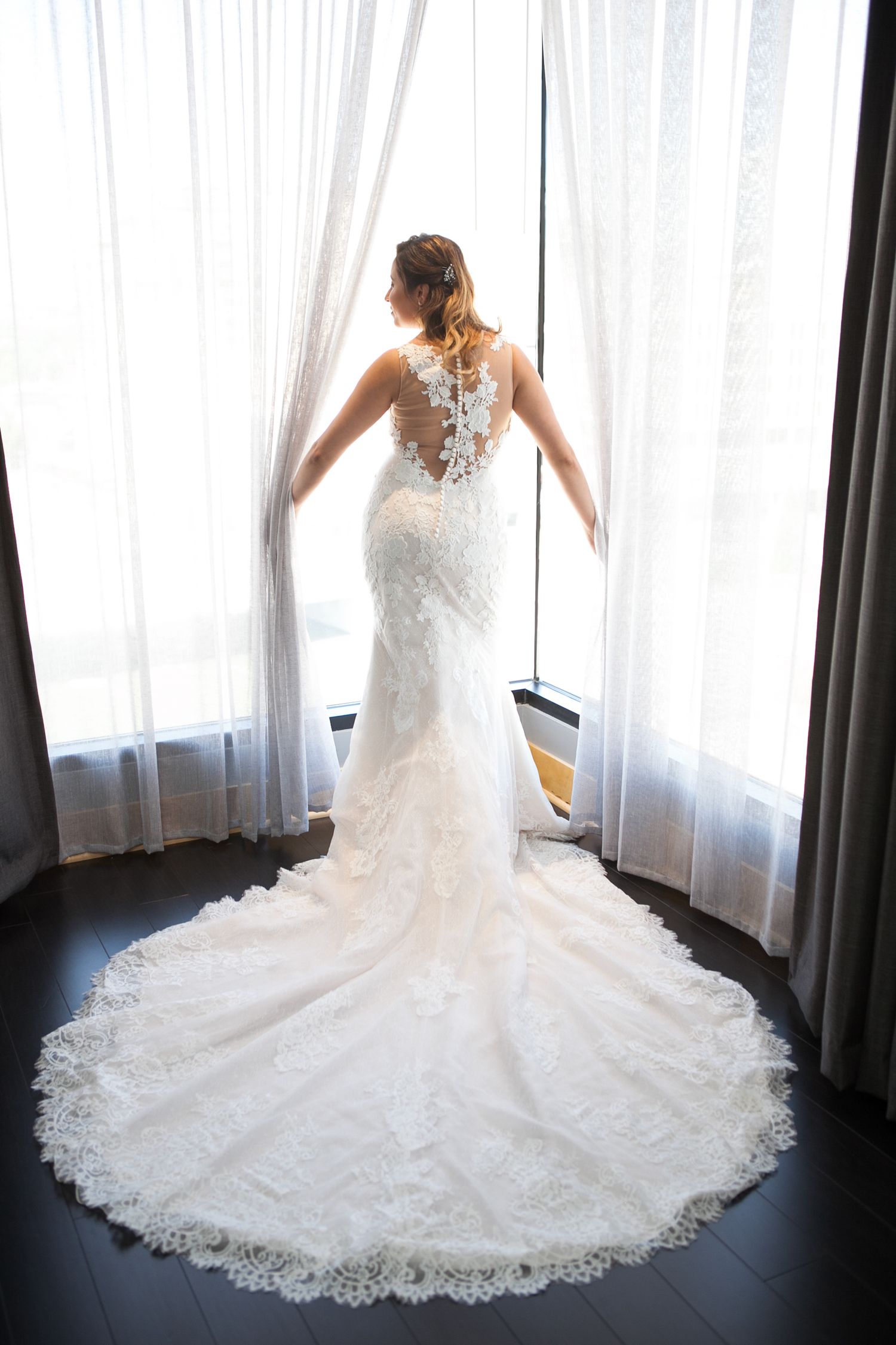 Wedding dress with intricate lace train spread beautifully across dark wooden floor.