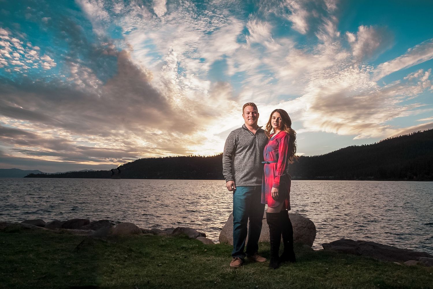 Couple embracing by mountain lake during dramatic sunset with blue and orange sky in Lake Tahoe.
