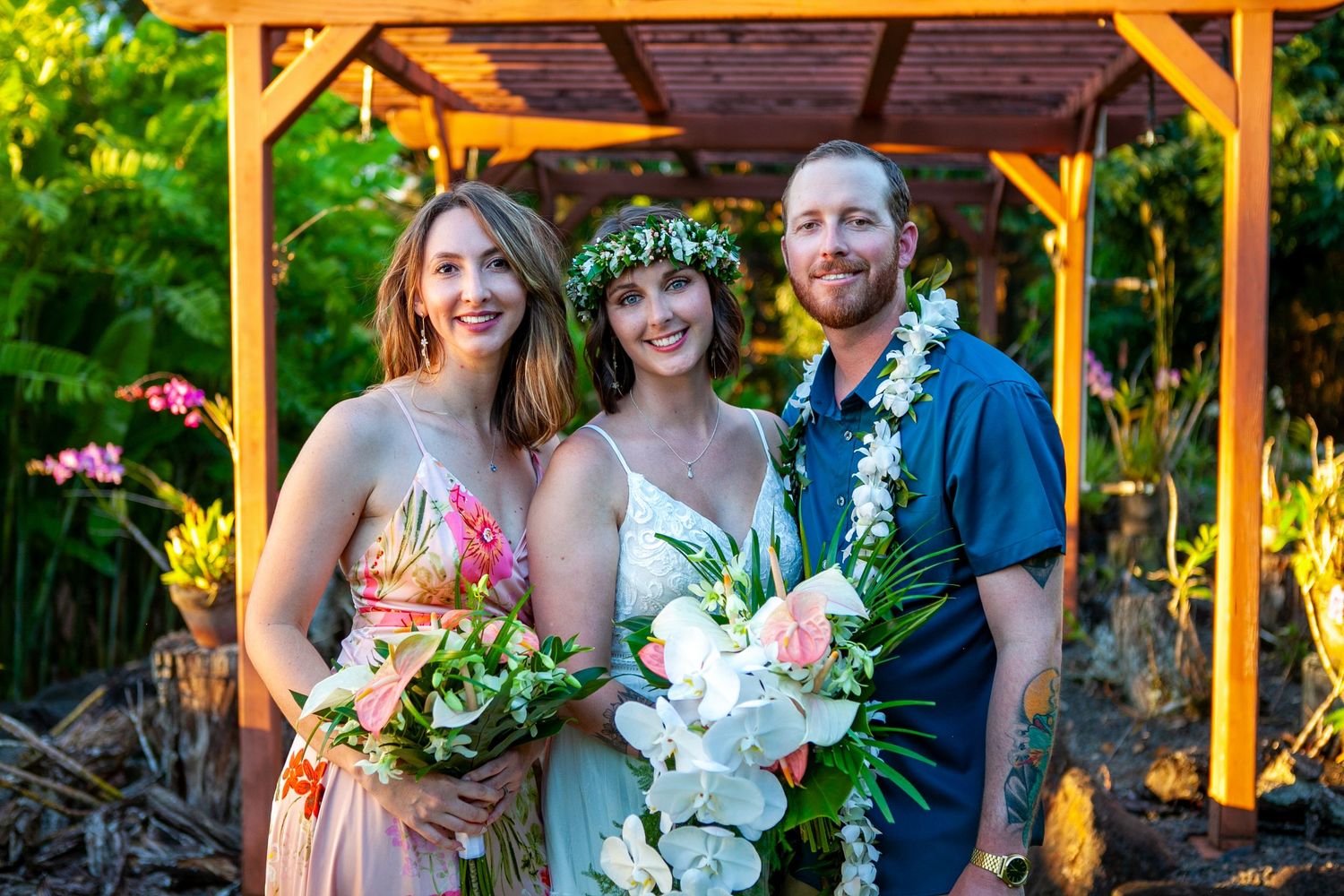 Wedding party poses under wooden pergola with lush greenery and flowers during golden hour sunset lighting in Kauai.