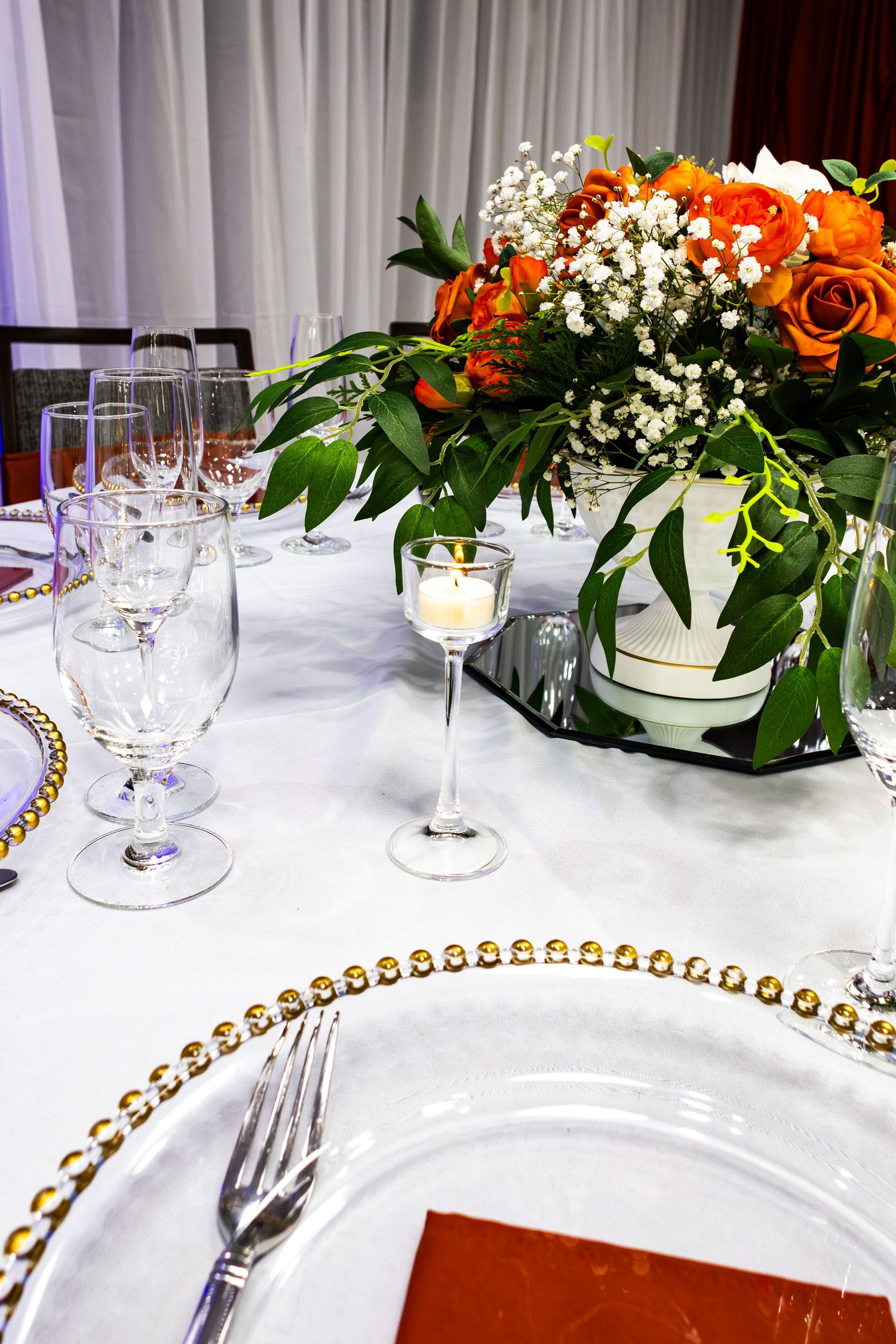 Elegant table setting with white linens, gold-rimmed plates, crystal glasses, and orange floral centerpieces at a formal event.