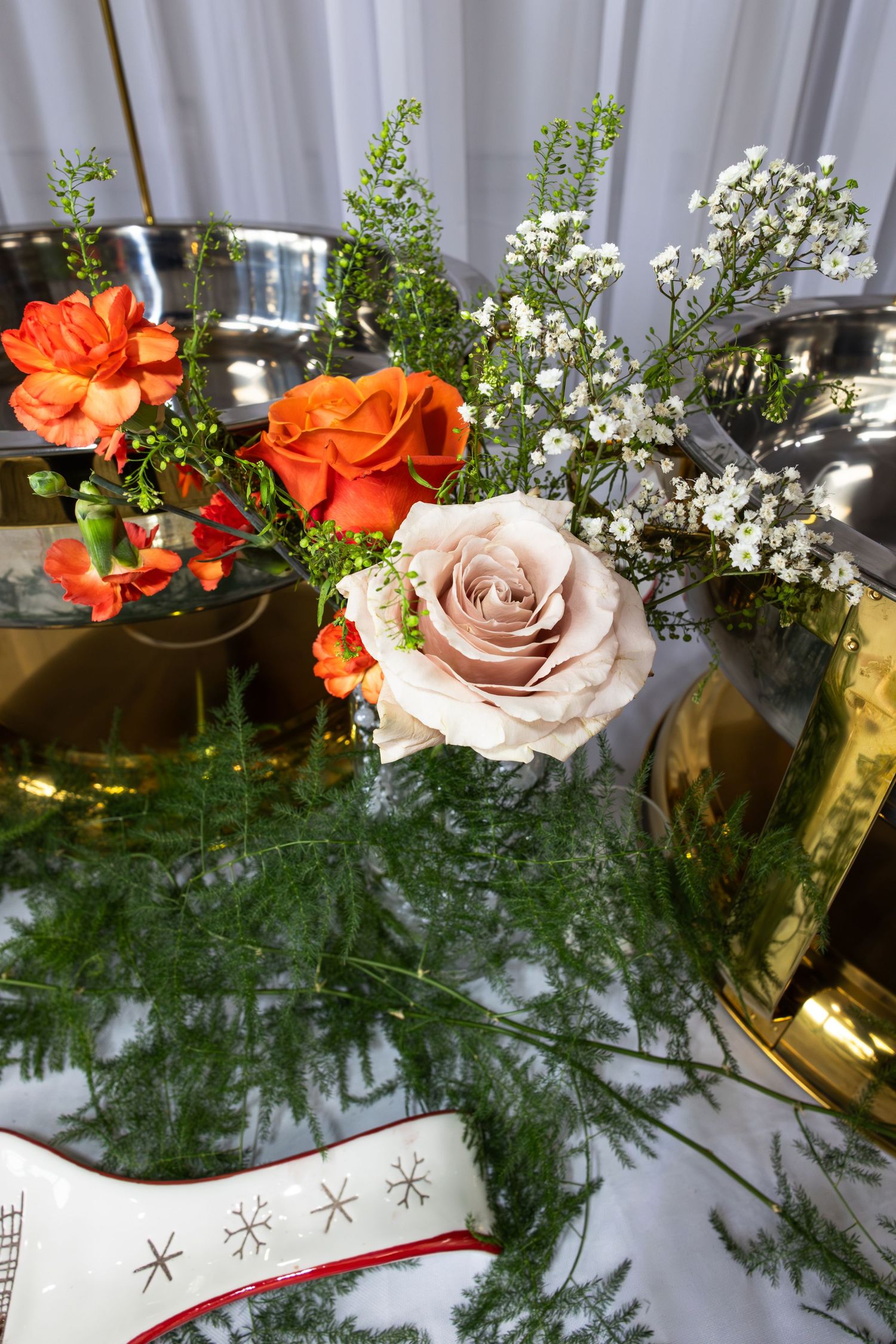Elegant floral centerpiece arrangement with orange and pink roses accented by delicate white flowers and greenery.