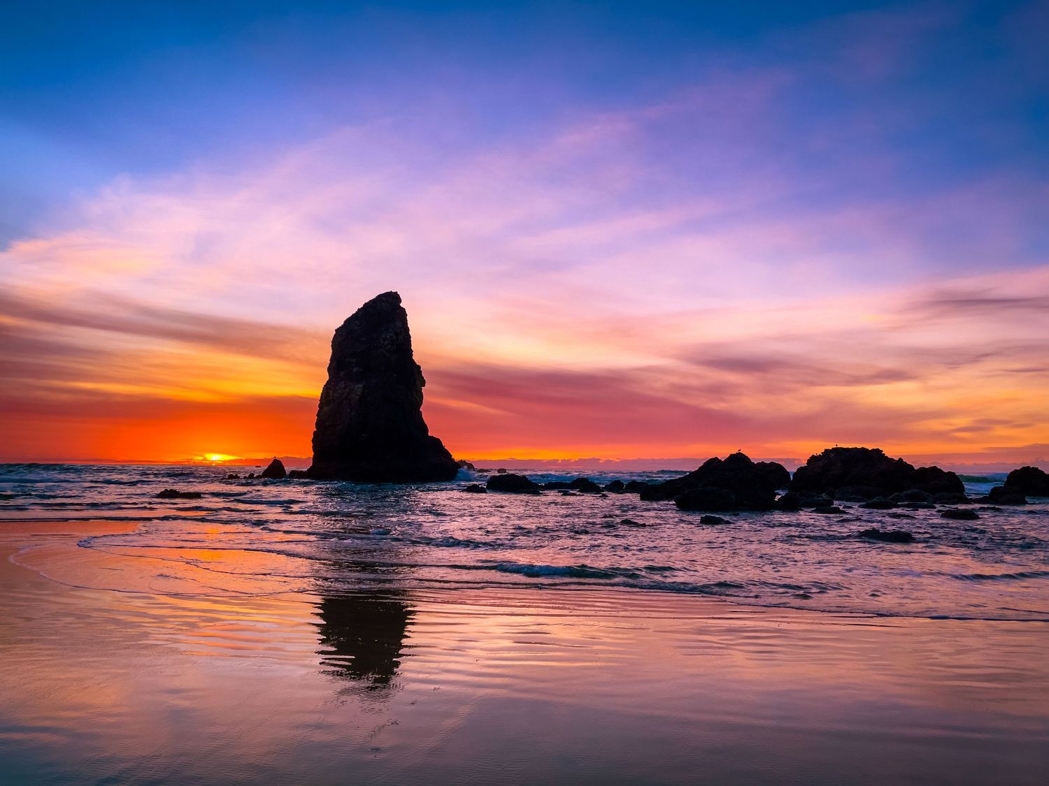 Landscape photography of dramatic coastal sunset with silhouetted rock formations and ocean waves in vibrant orange and purple hues.