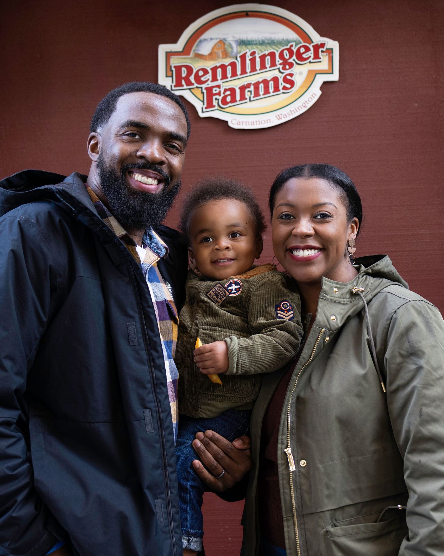 A family poses together in front of a Bemlinger Farms sign on a brick wall.