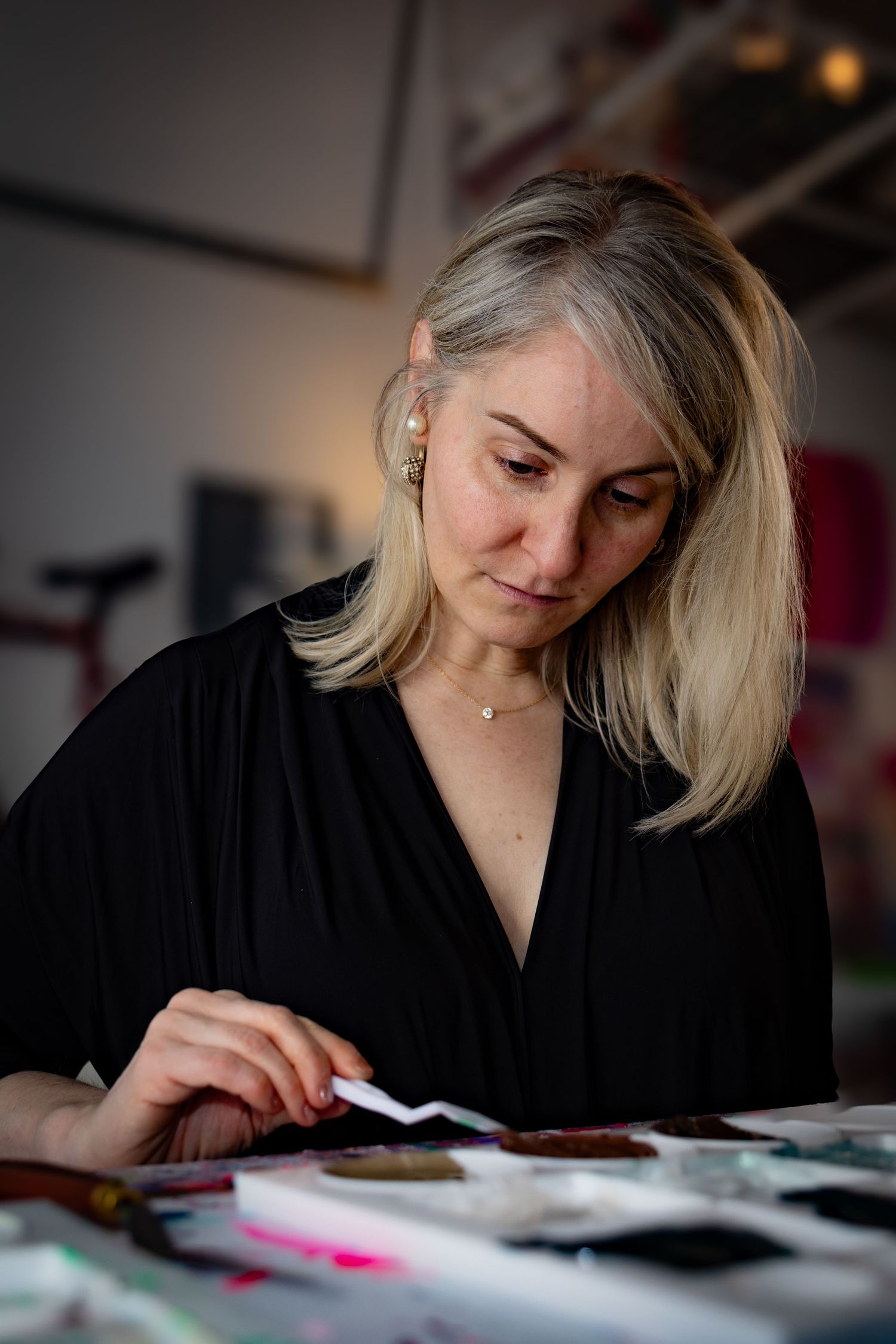 Person in black shirt focused on creative work at desk with art supplies and papers.