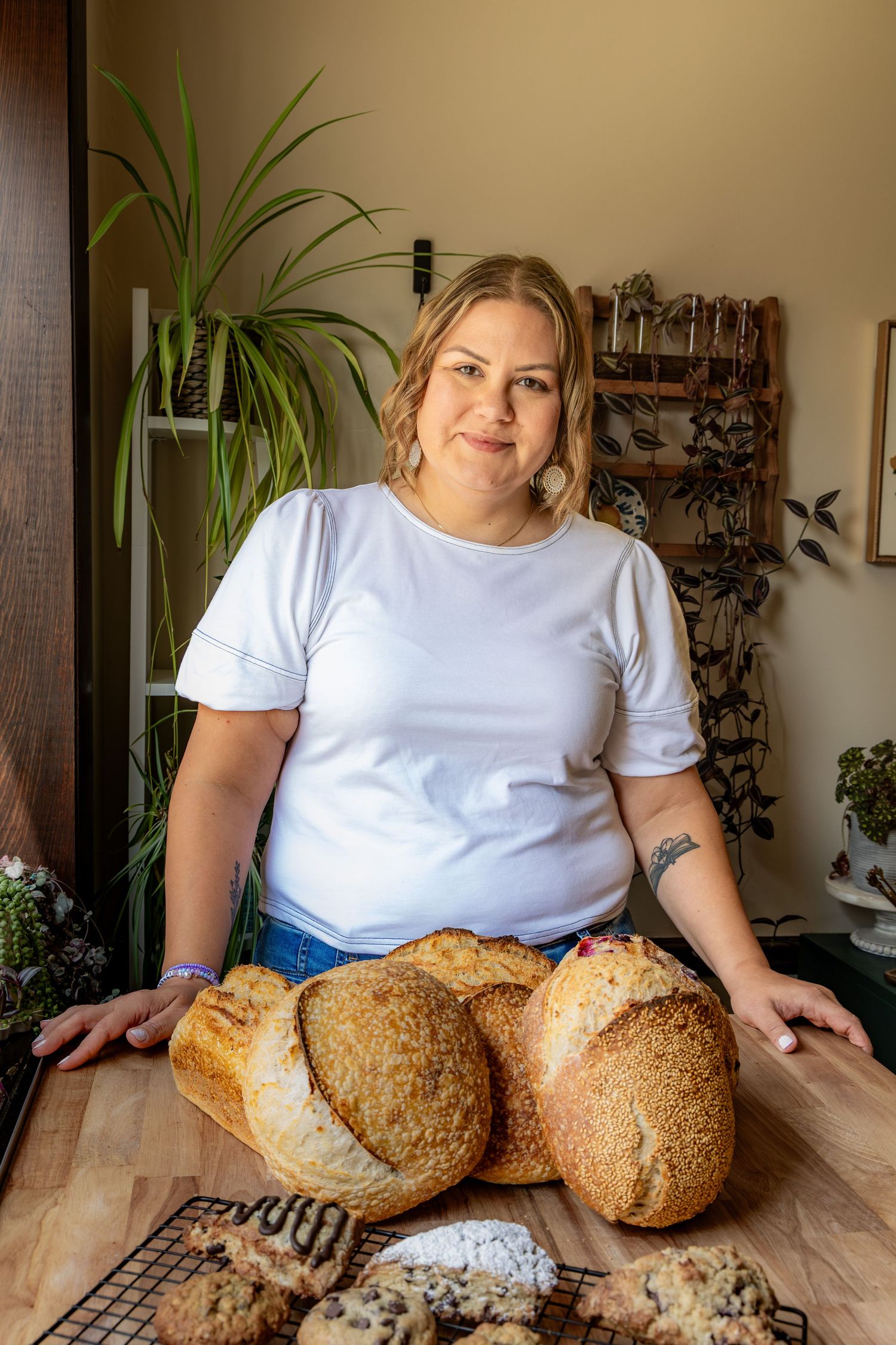 Woman baker proudly displays freshly baked artisan sourdough bread loaves on a wooden counter in a cozy home kitchen.