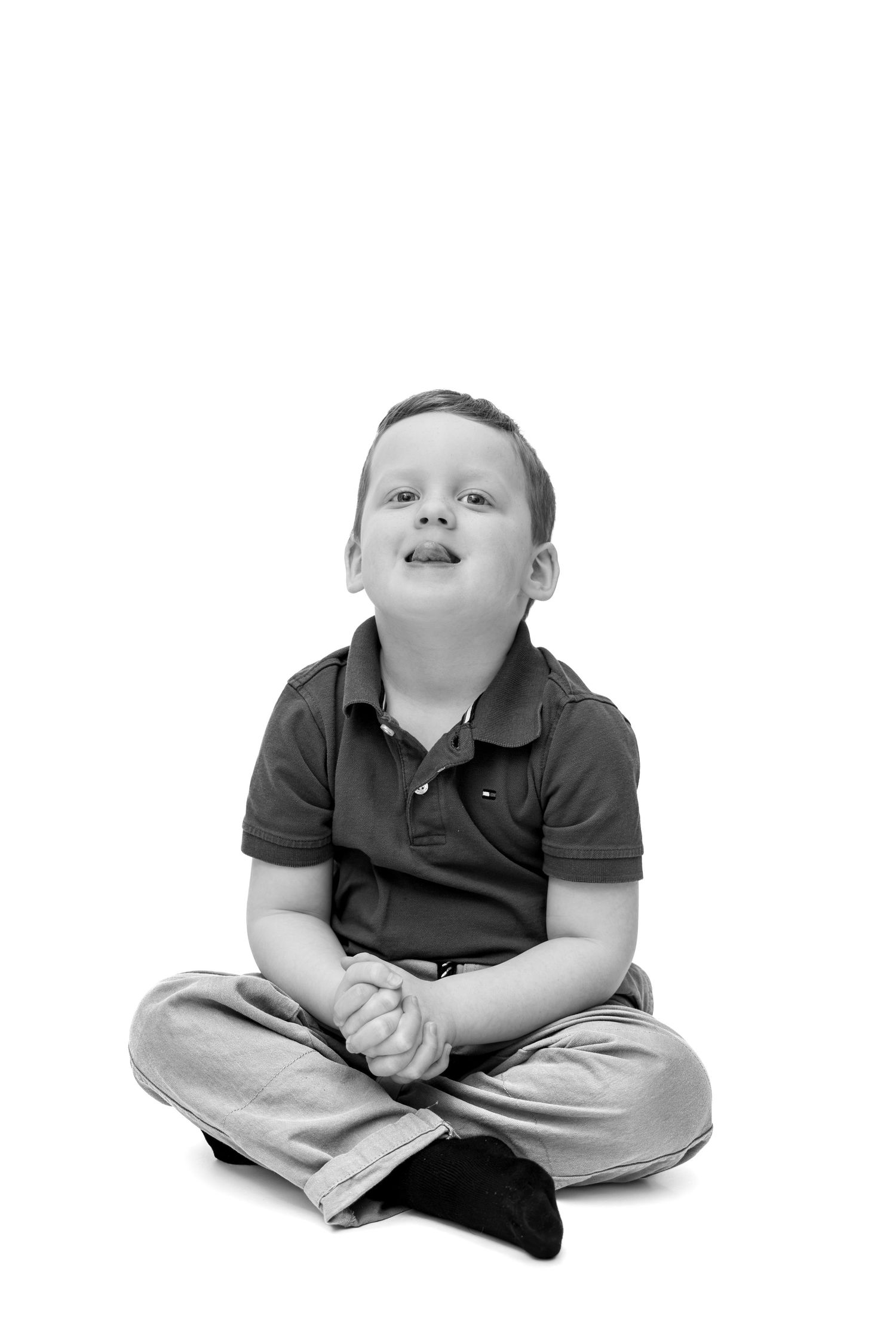 Black and white photo of a young boy sitting cross-legged on the floor, looking up with a smile.