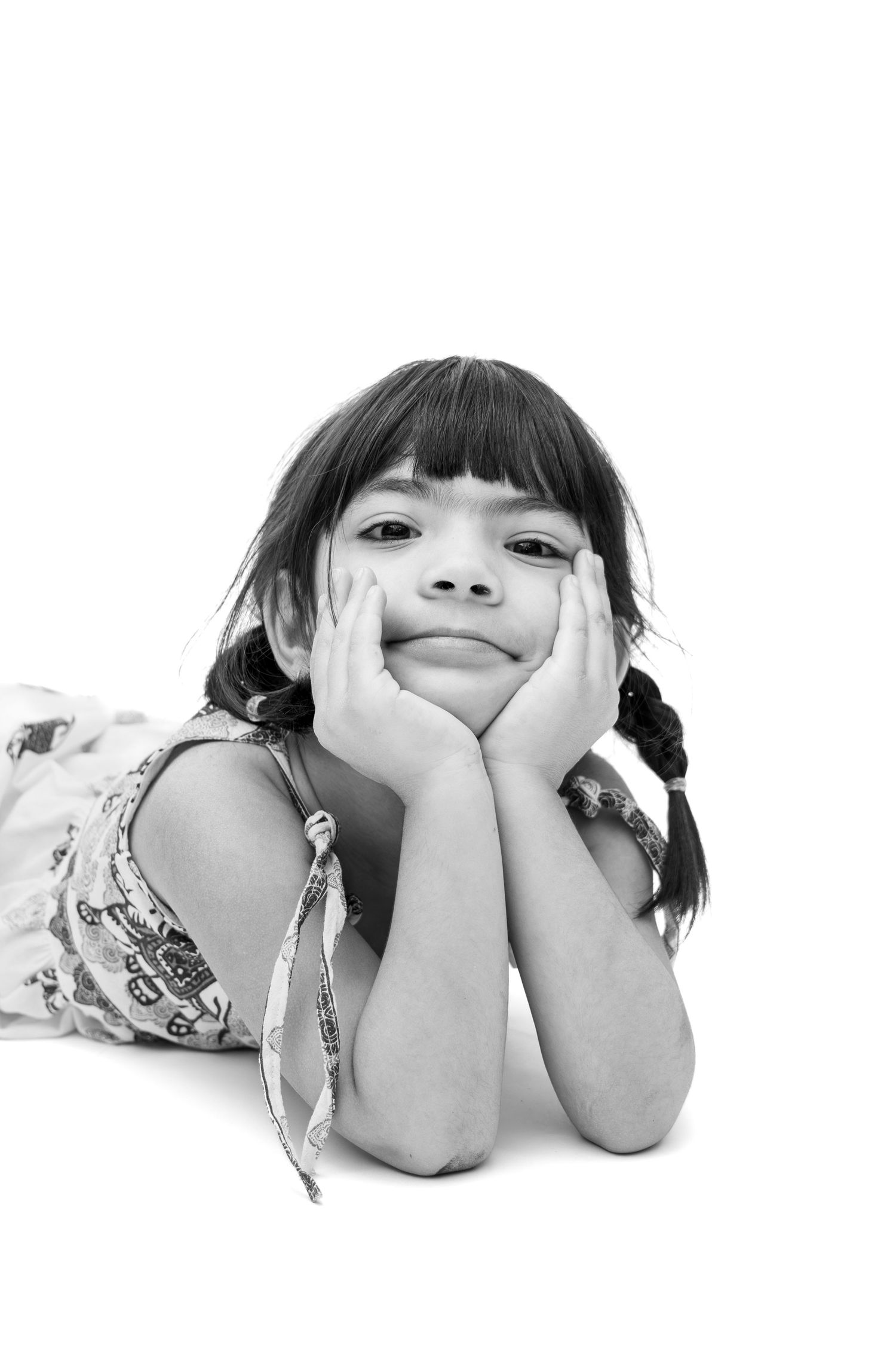 Black and white portrait of a young girl with braids resting her chin on her hands, smiling at the camera.
