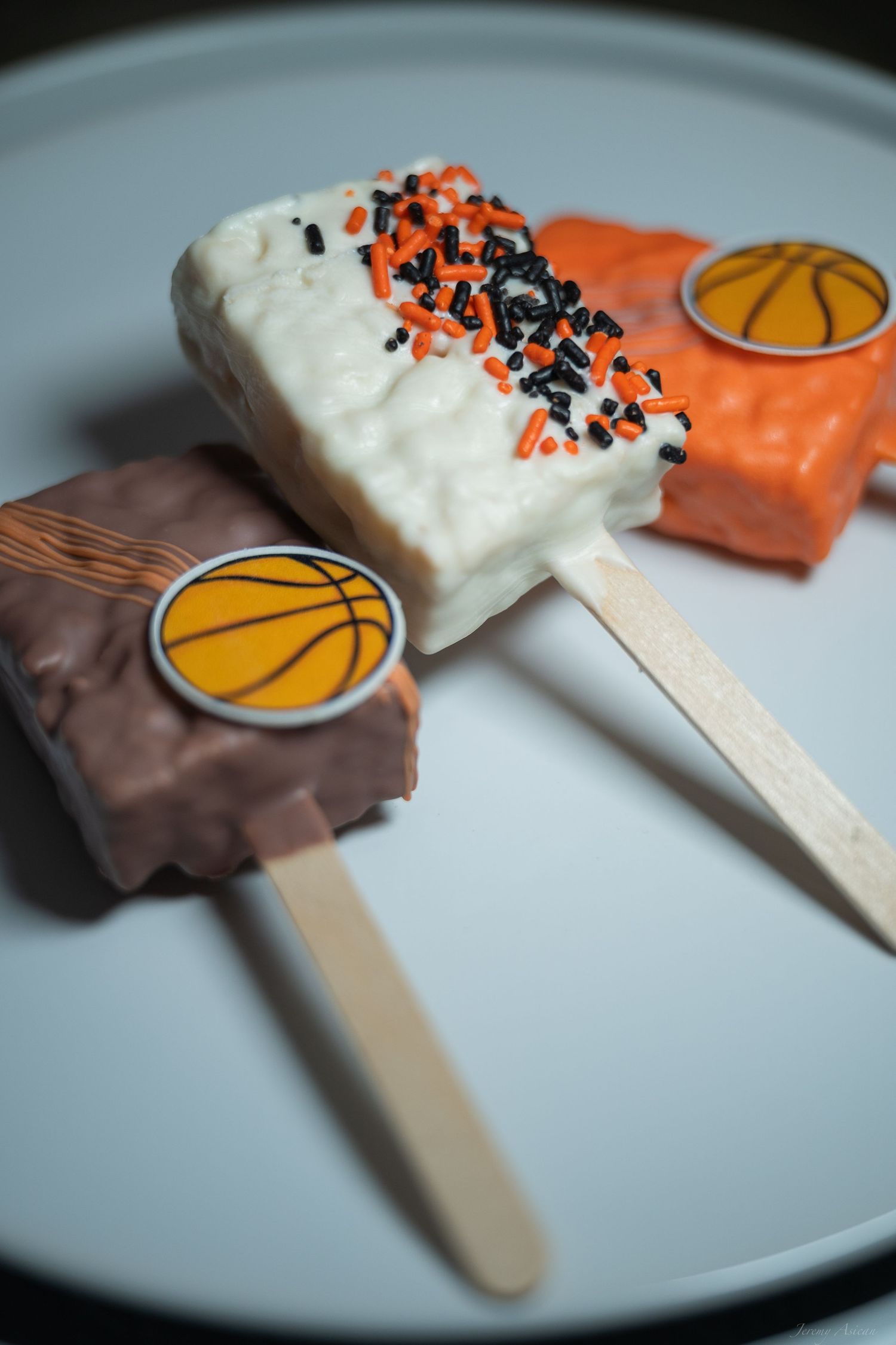 Three basketball-themed cake pops in chocolate, white, and orange coatings with sprinkles on a gray plate. Stockton photographer