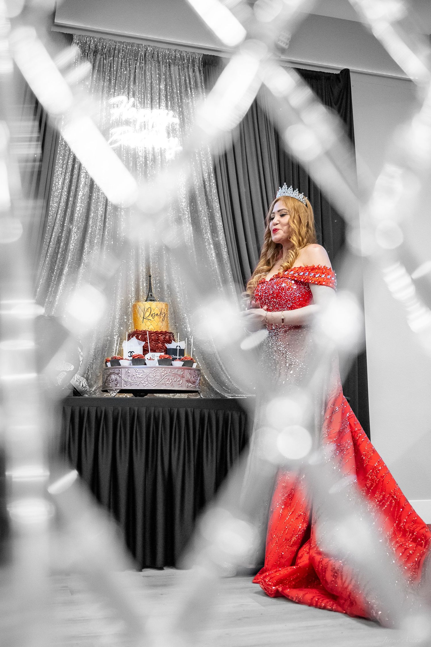 A woman in a red gown and crown poses beside a decorated birthday cake at an elegant celebration. Stockton photographer