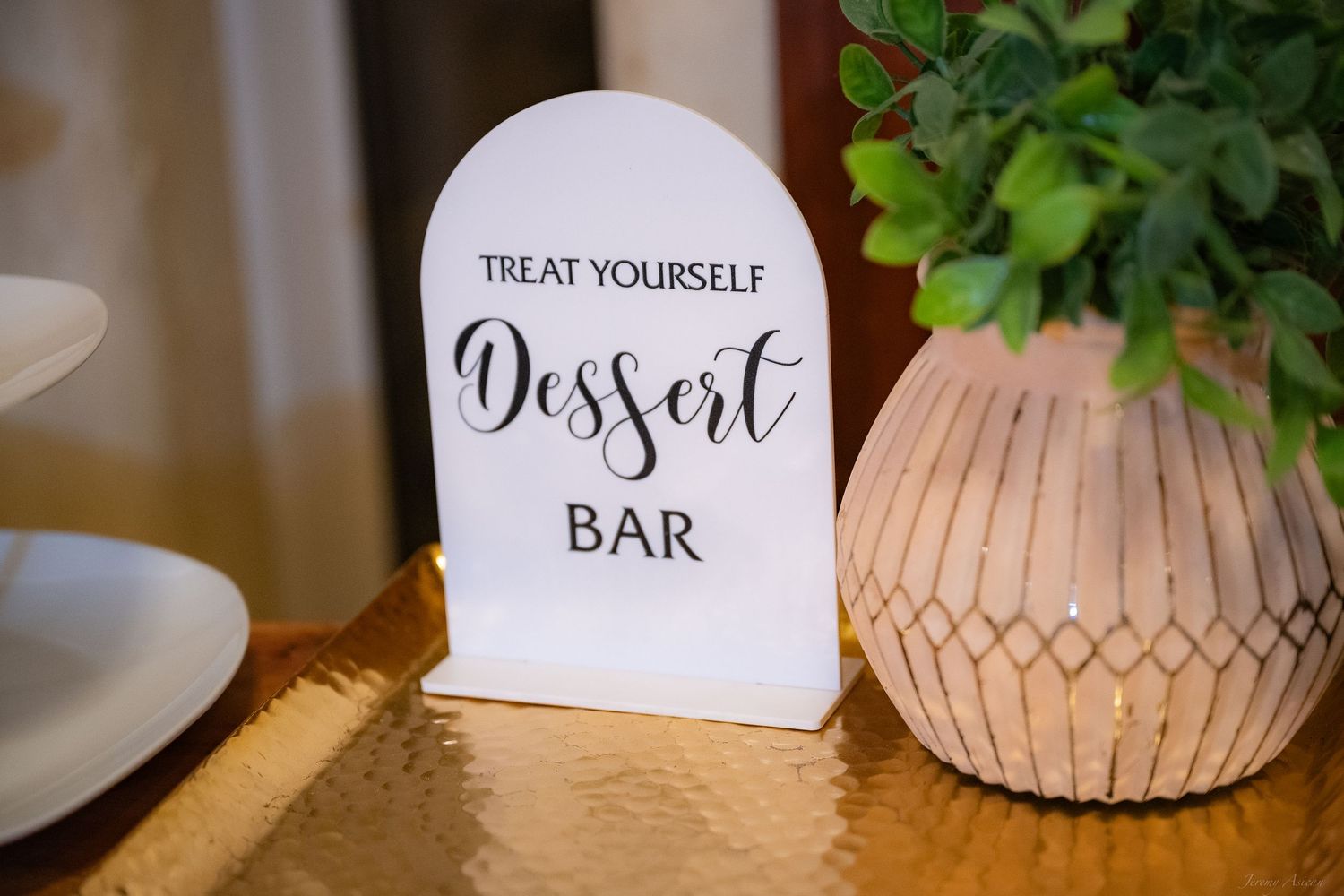 White arched dessert bar sign reading Treat Yourself on a gold tray beside a wooden geometric candle holder.