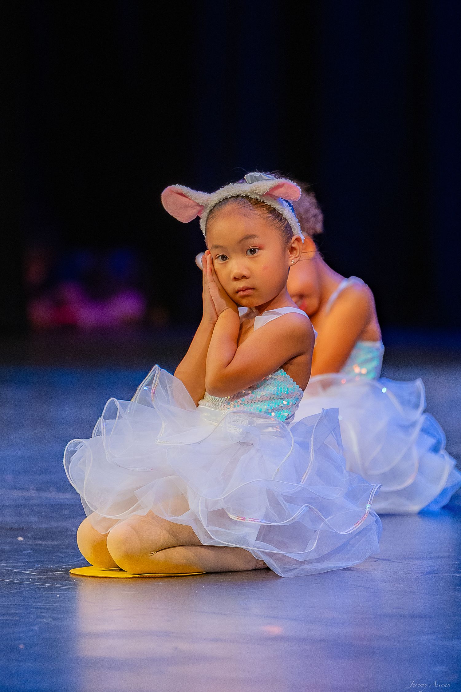 Young girl in white tutu and mouse ears sits on stage during a ballet recital performance. Stockton photographer