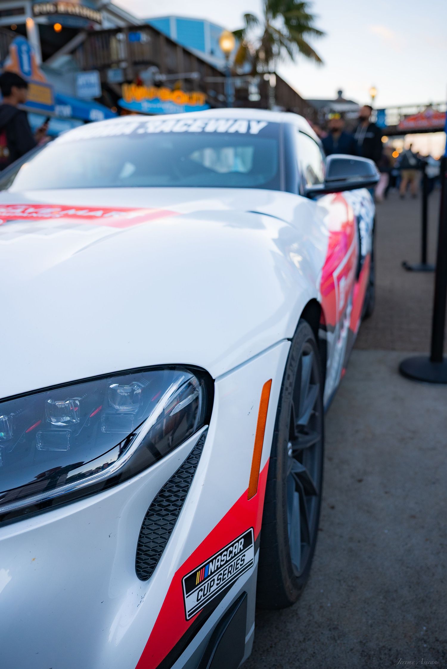 White race car with red and black decals parked at a raceway event, featuring aerodynamic design and sponsor logos. Stockton photographer