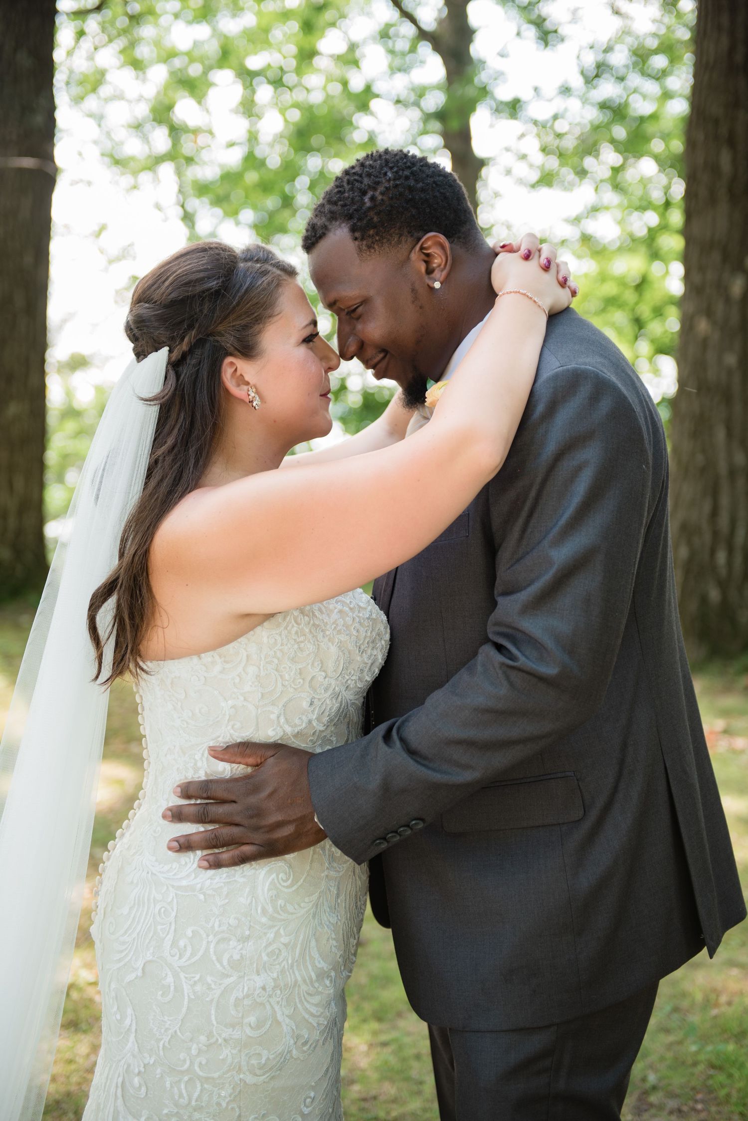 Interracial bride and groom embrace forehead-to-forehead in romantic outdoor wedding portrait.