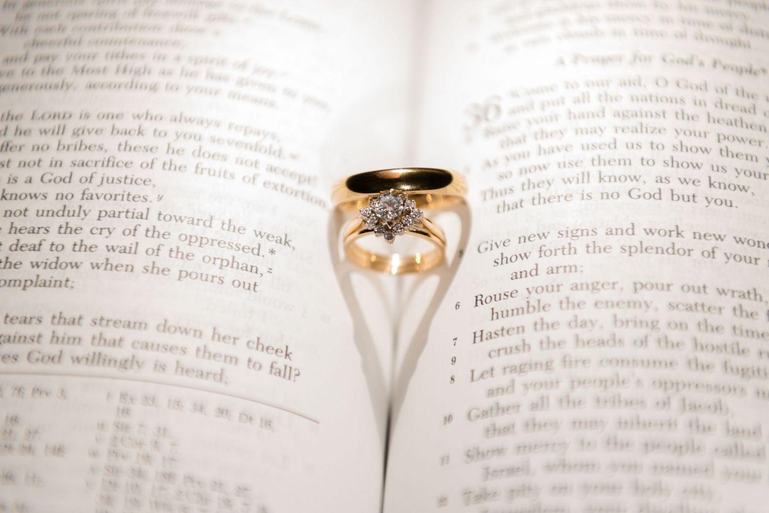 Gold star-shaped diamond ring placed in an open Bible, casting a heart-shaped shadow on the pages.