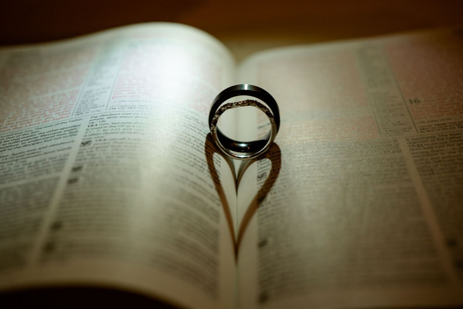Wedding ring casting a heart-shaped shadow on an open Bible page in romantic lighting.