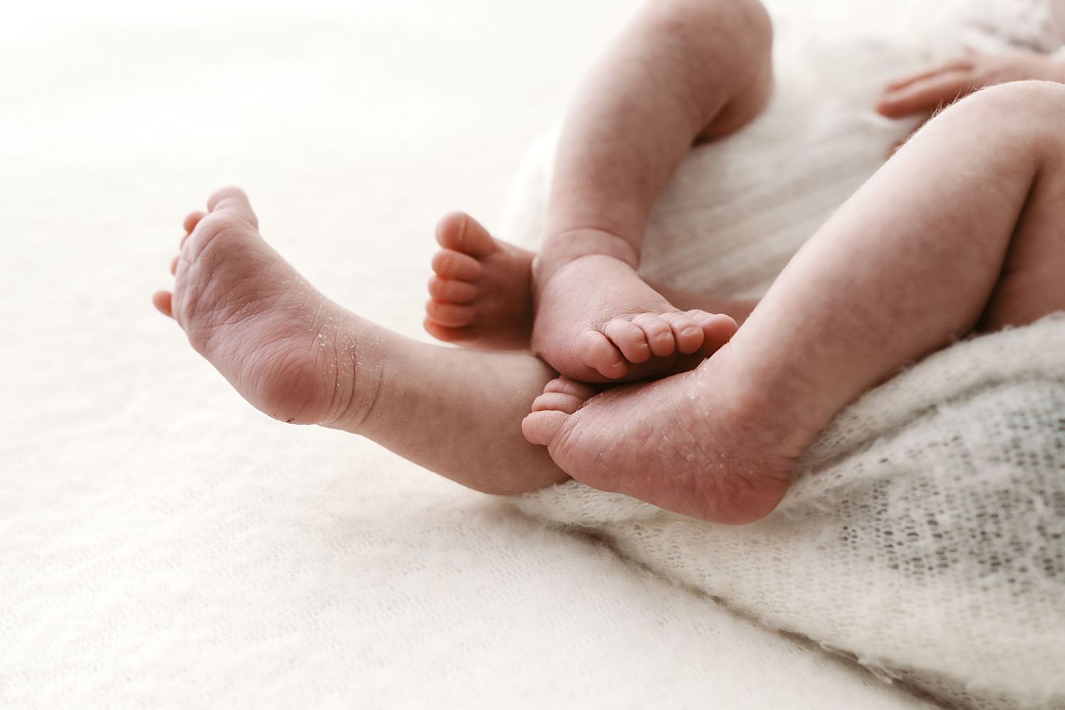Close-up of tiny newborn baby feet and toes resting on soft white blanket.