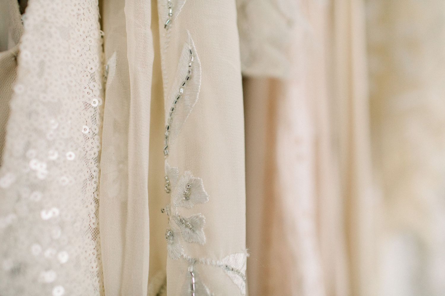Row of elegant white and cream sequin bridal gowns hanging on a rack.