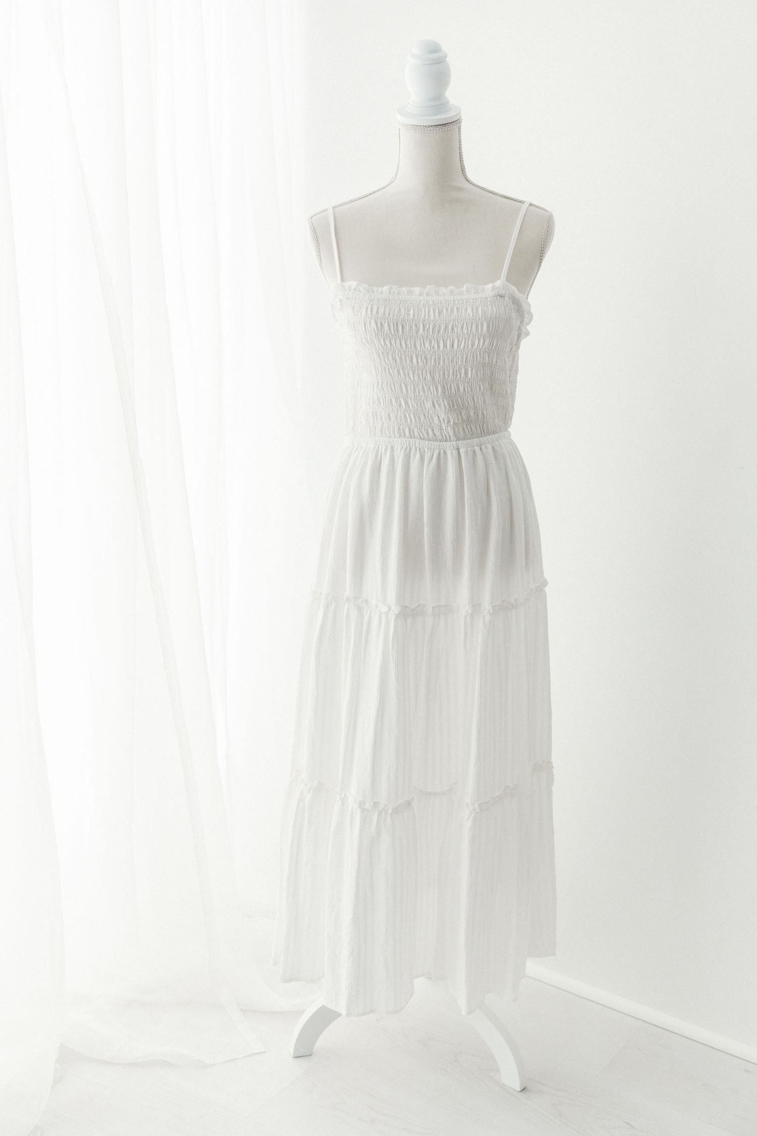 White spaghetti strap smocked bodice tiered chiffon maxi dress on mannequin.