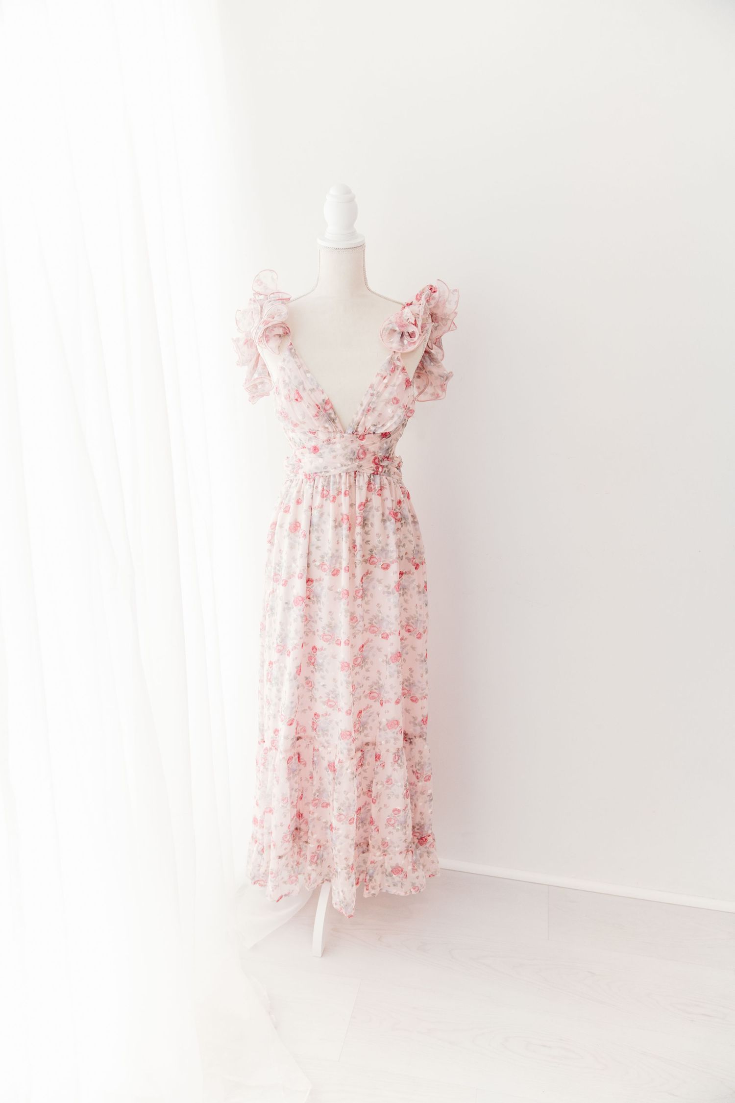 Pink floral ruffle shoulder wrap maxi dress with tie waist on white mannequin.