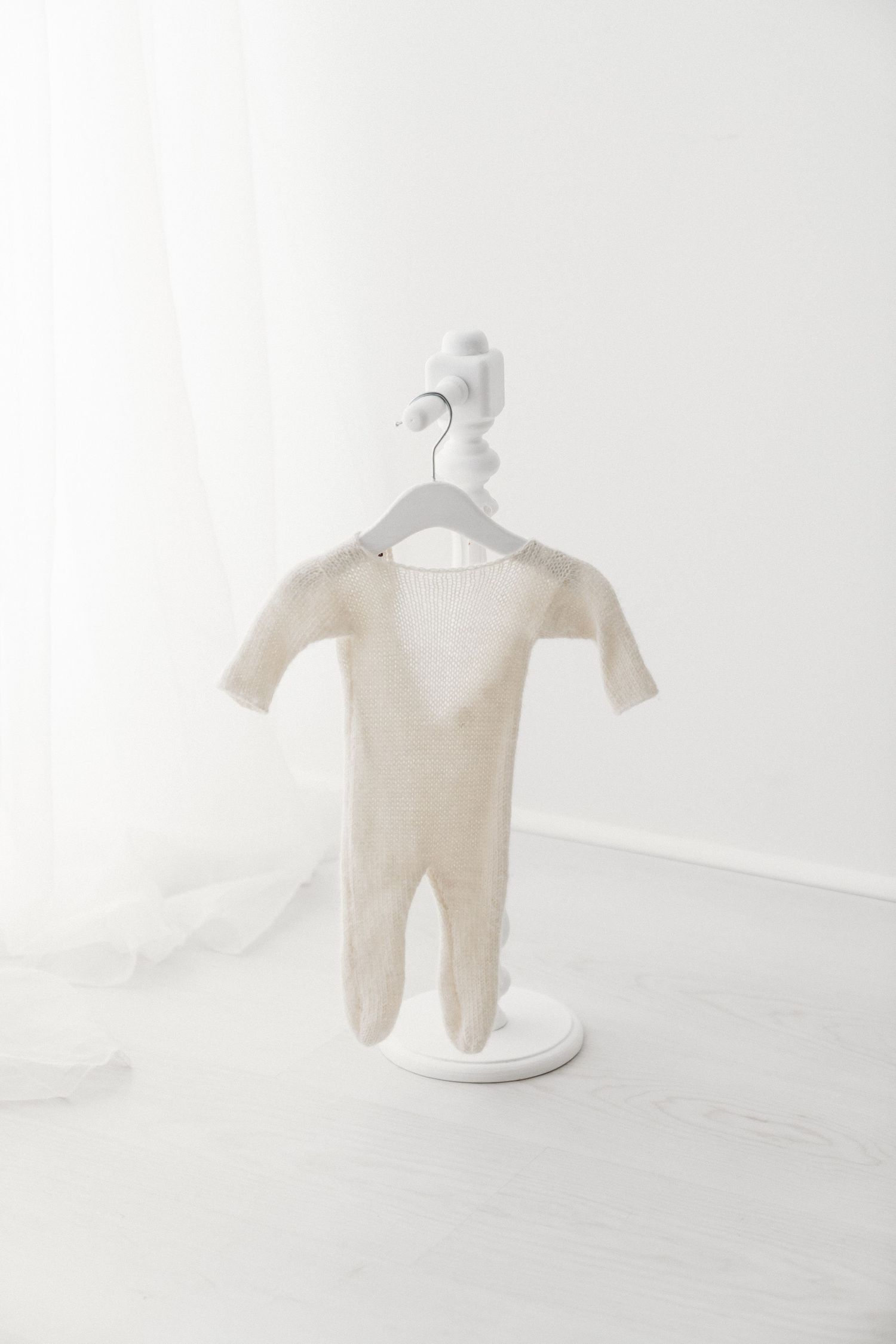 Neutral beige knit newborn footie onesie displayed on a miniature white mannequin stand in studio.