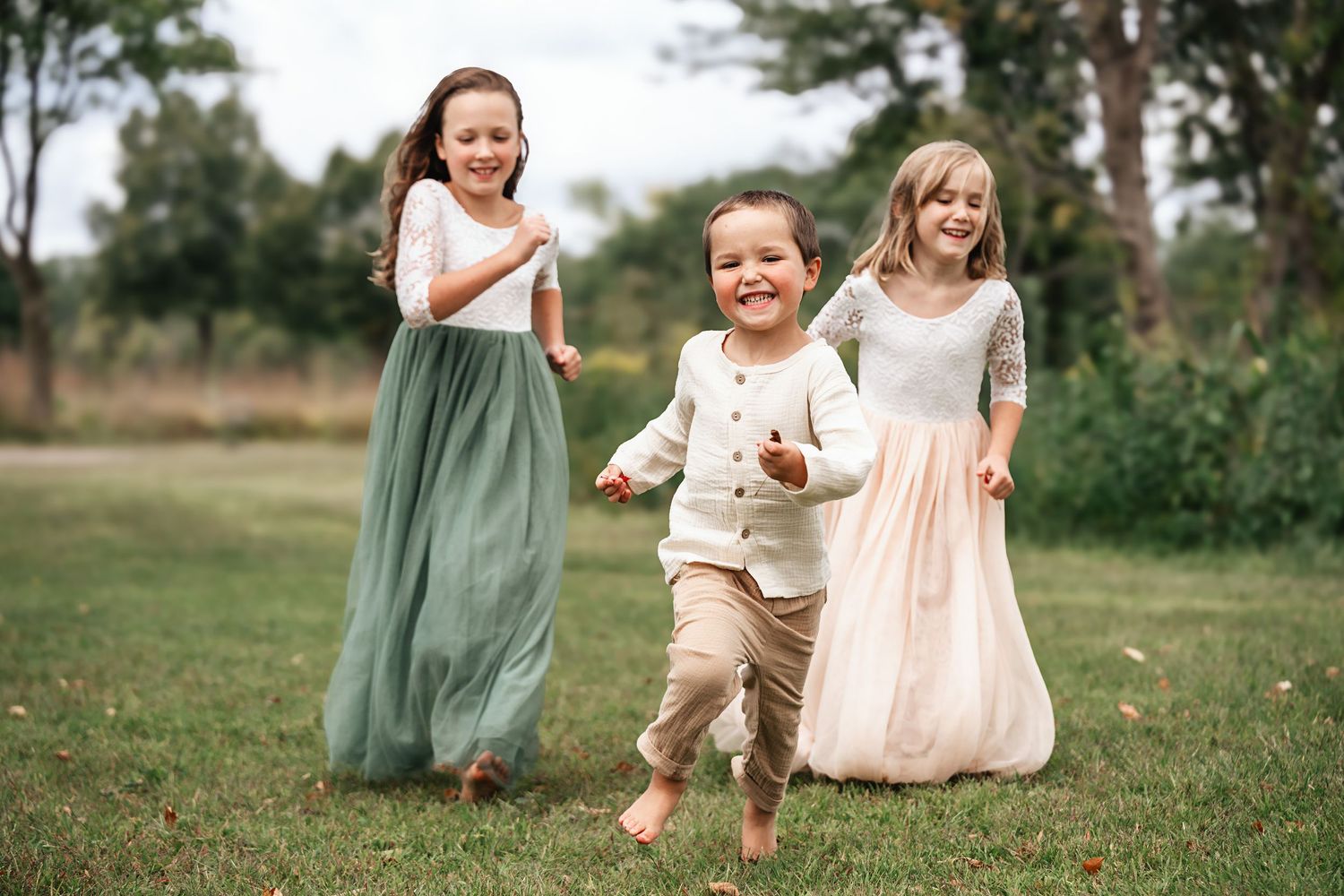 Three happy children running and playing on green grass in nature outfits.