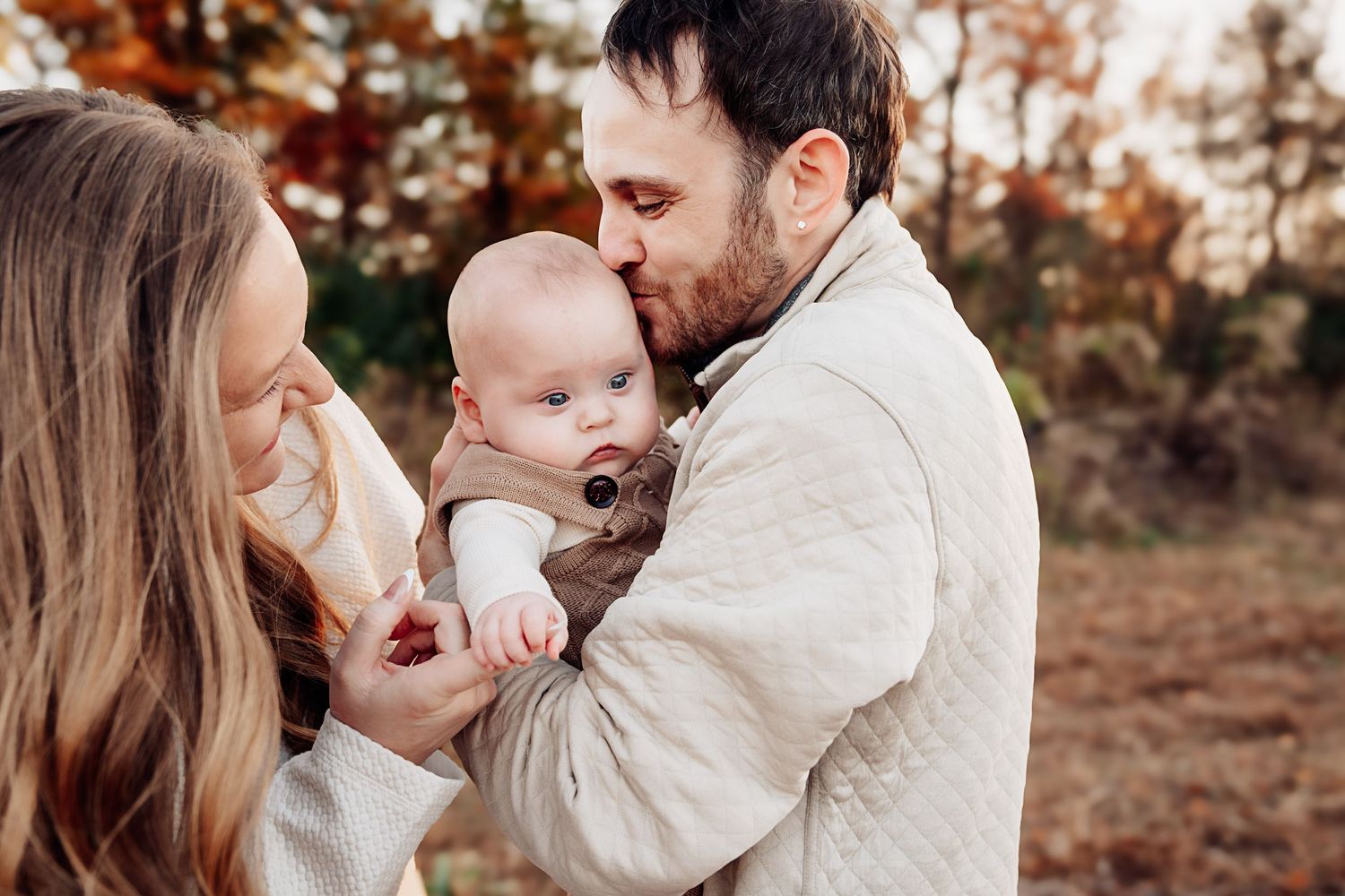Parents kissing their newborn baby outdoors during a fall family photo session.