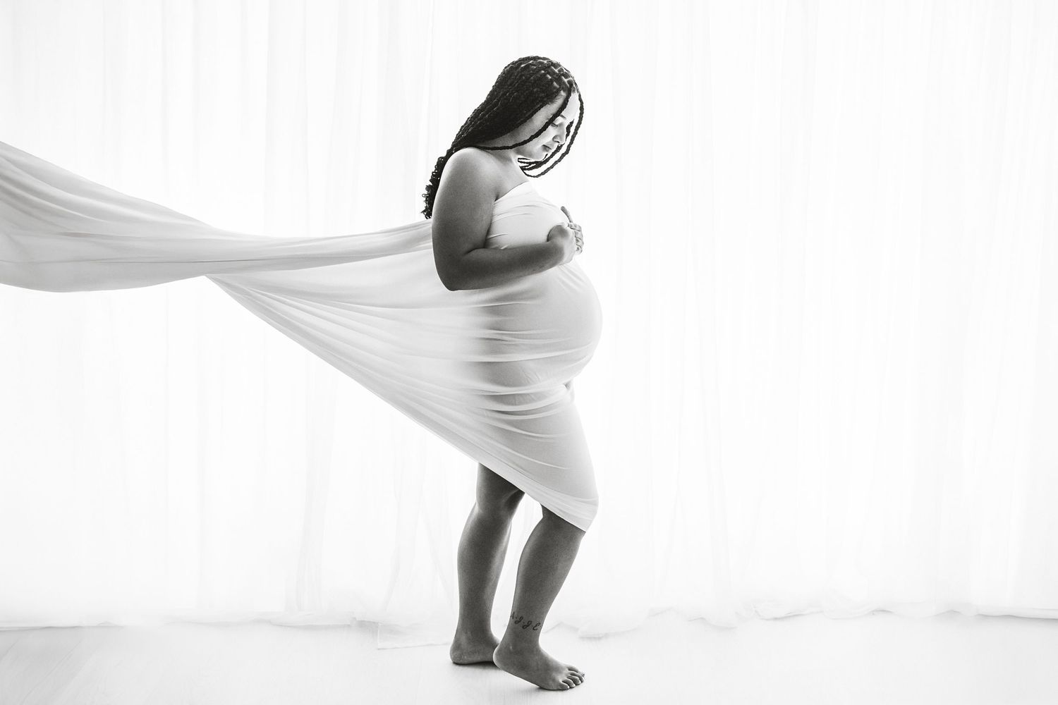 Black and white maternity photo of pregnant woman draped in flowing white fabric.