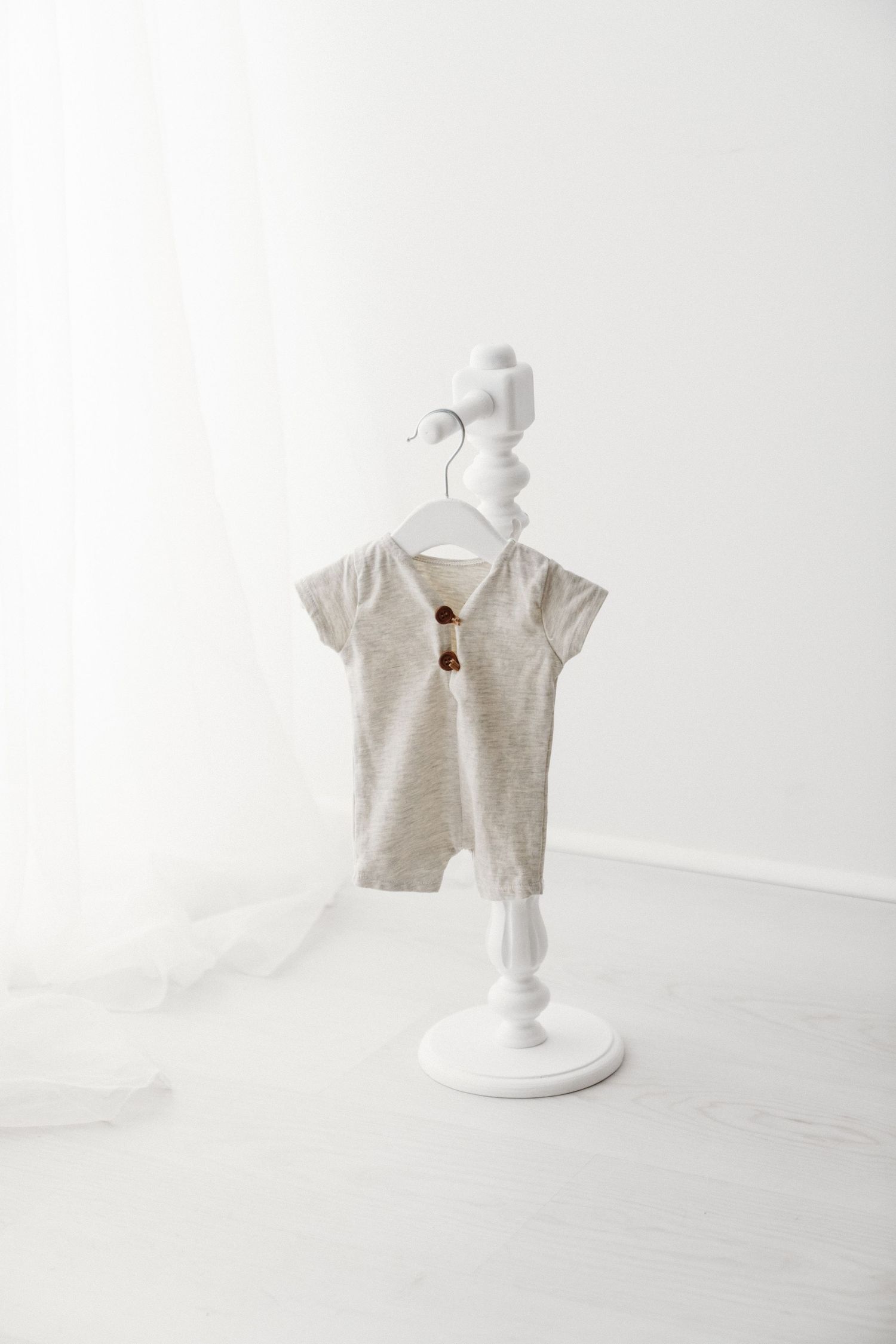 Beige baby romper with brown buttons displayed on a white decorative stand against a white background.