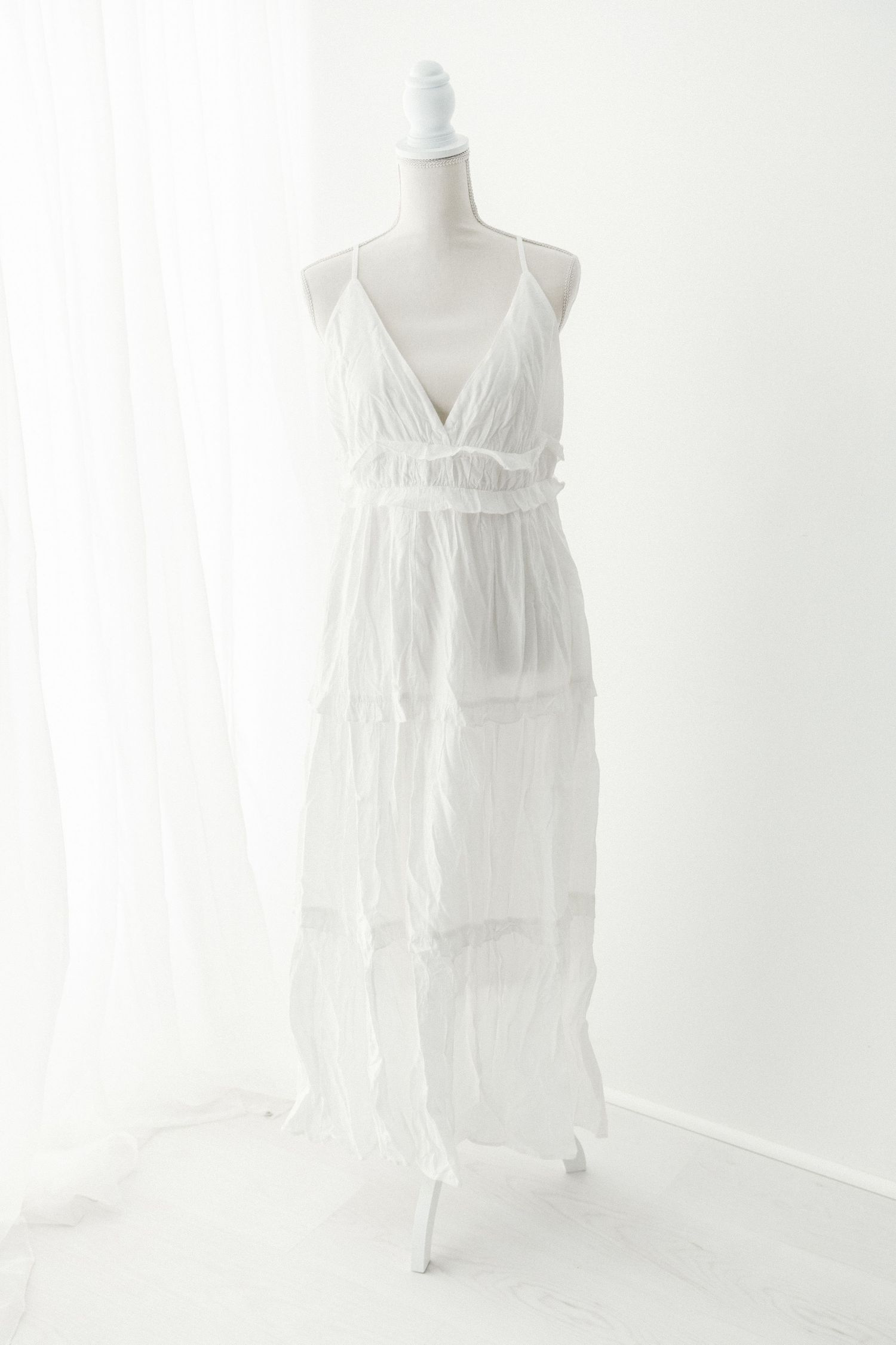 Sleeveless white tiered maxi dress with V-neckline and spaghetti straps displayed on a mannequin.