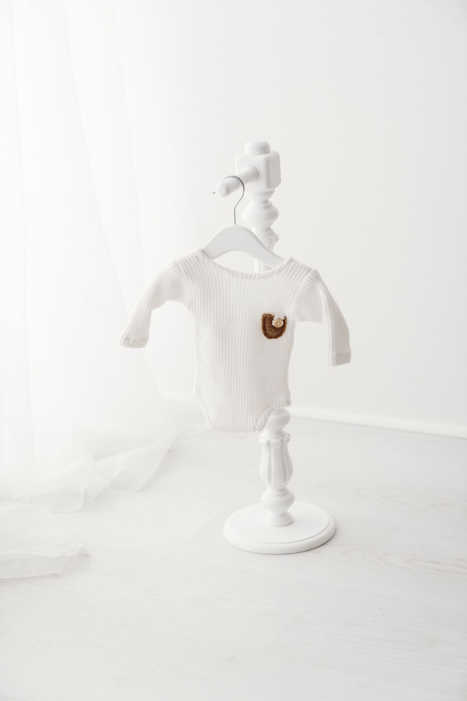 White ribbed long-sleeve baby bodysuit with donut patch on a white decorative hanger stand.