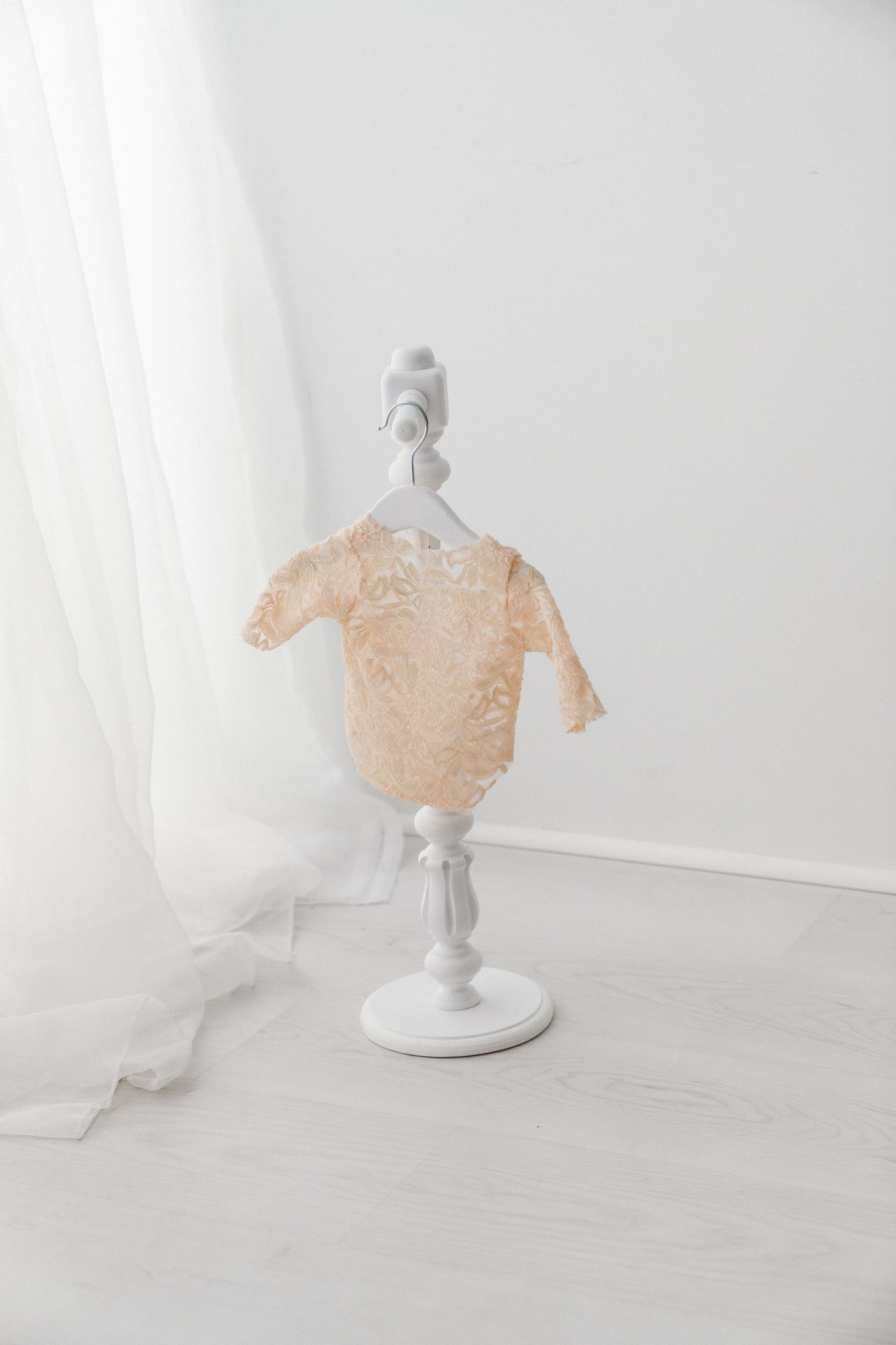 Delicate beige lace baby bodysuit displayed on a miniature white mannequin stand against a white background.