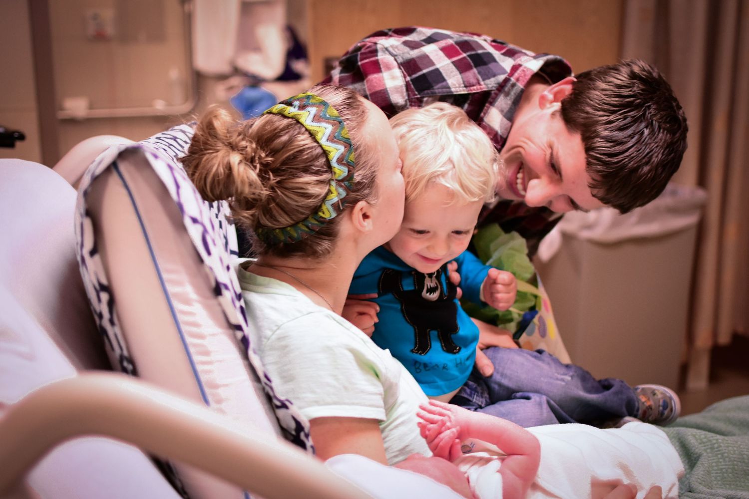 Family with toddler meeting their newborn sibling for the first time in a hospital room.