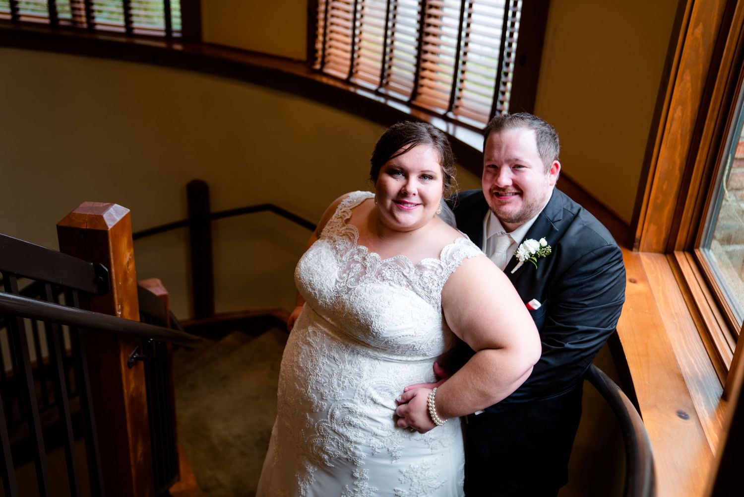 Smiling bride and groom posing together on a staircase inside a rustic wooden venue.