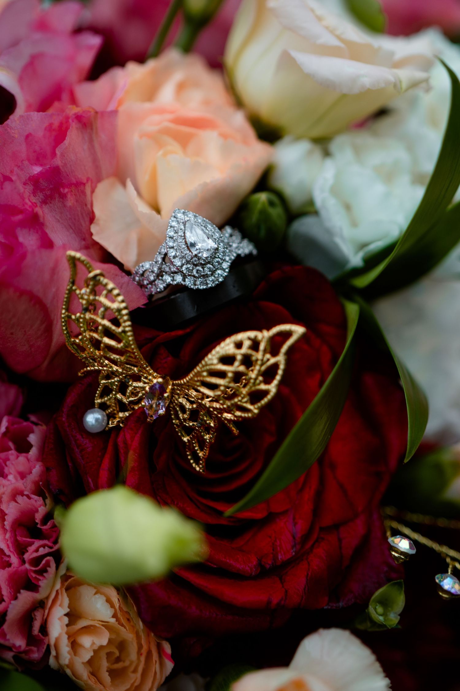 Diamond halo engagement ring and gold butterfly brooch resting on a colorful bridal bouquet.