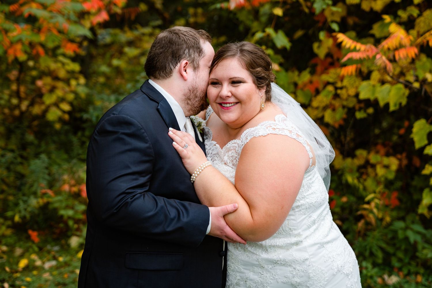 Bride and groom embrace joyfully before stunning red and orange autumn foliage in outdoor portrait.